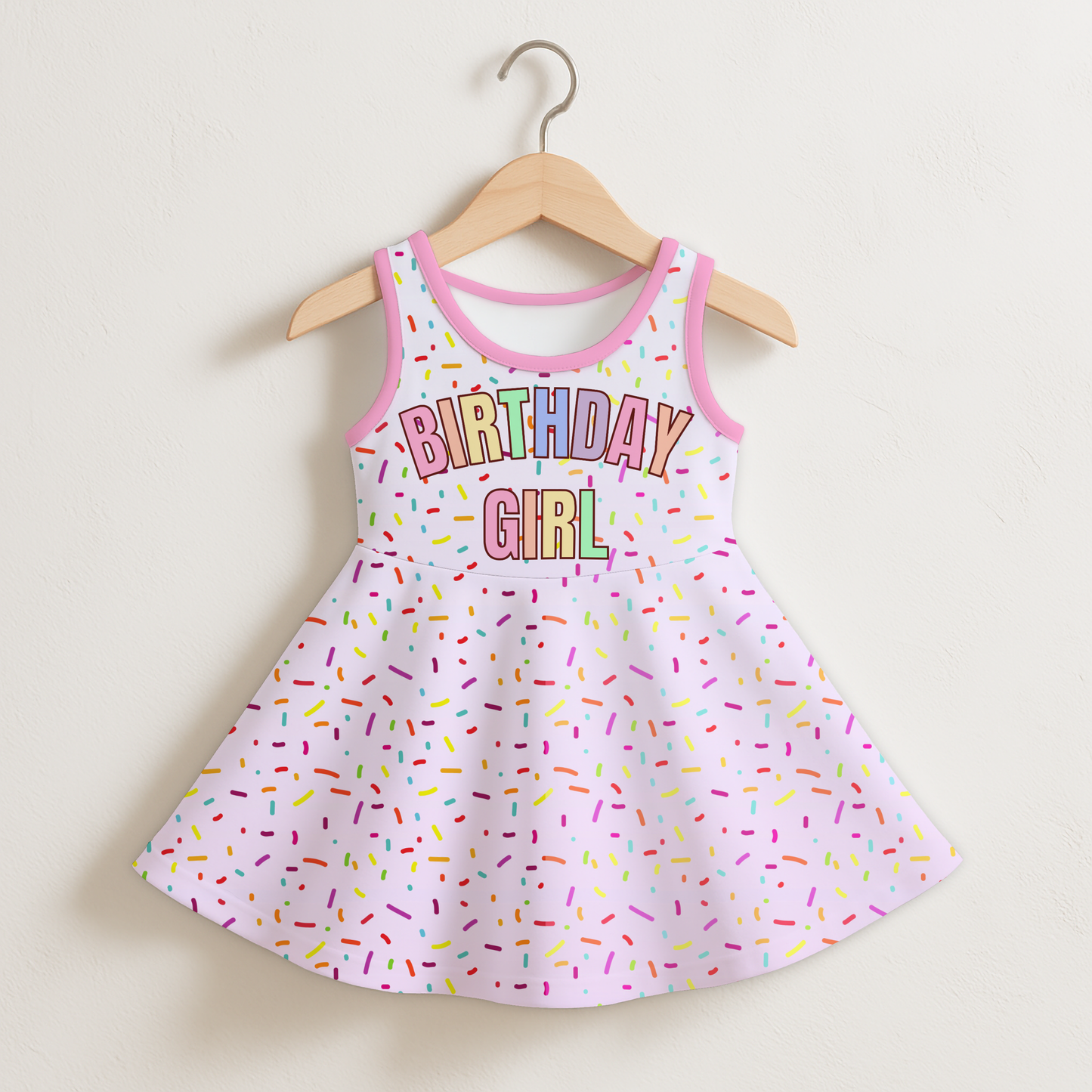 Children's dress with 'Birthday Girl' text and sprinkles on a hanger against a beige background