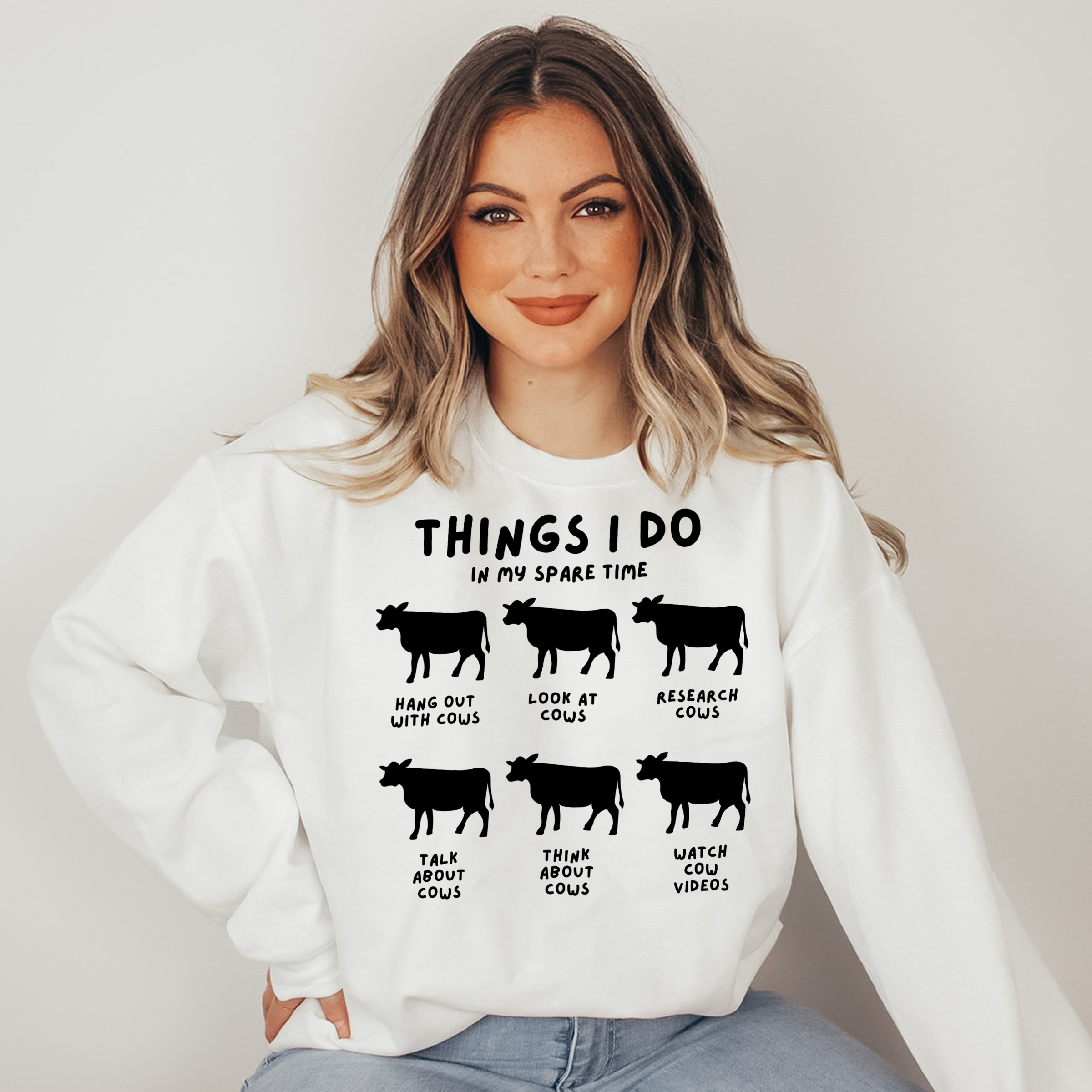 Woman wearing a white sweatshirt with cow-themed text design on a plain background