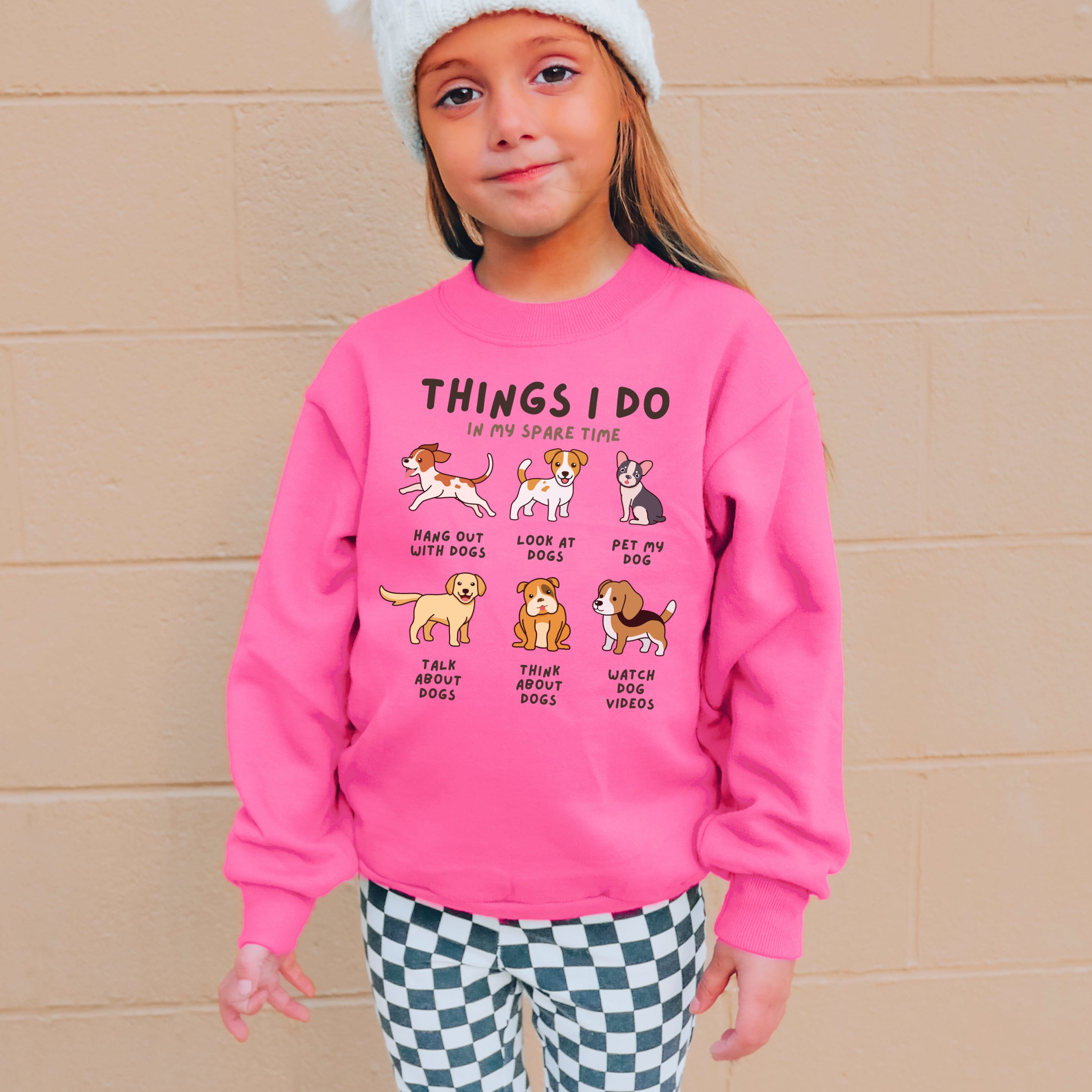 A child wearing a pink sweatshirt with text and illustrations of dogs, indicating favorite activities 'Things I Do In My Spare Time'.