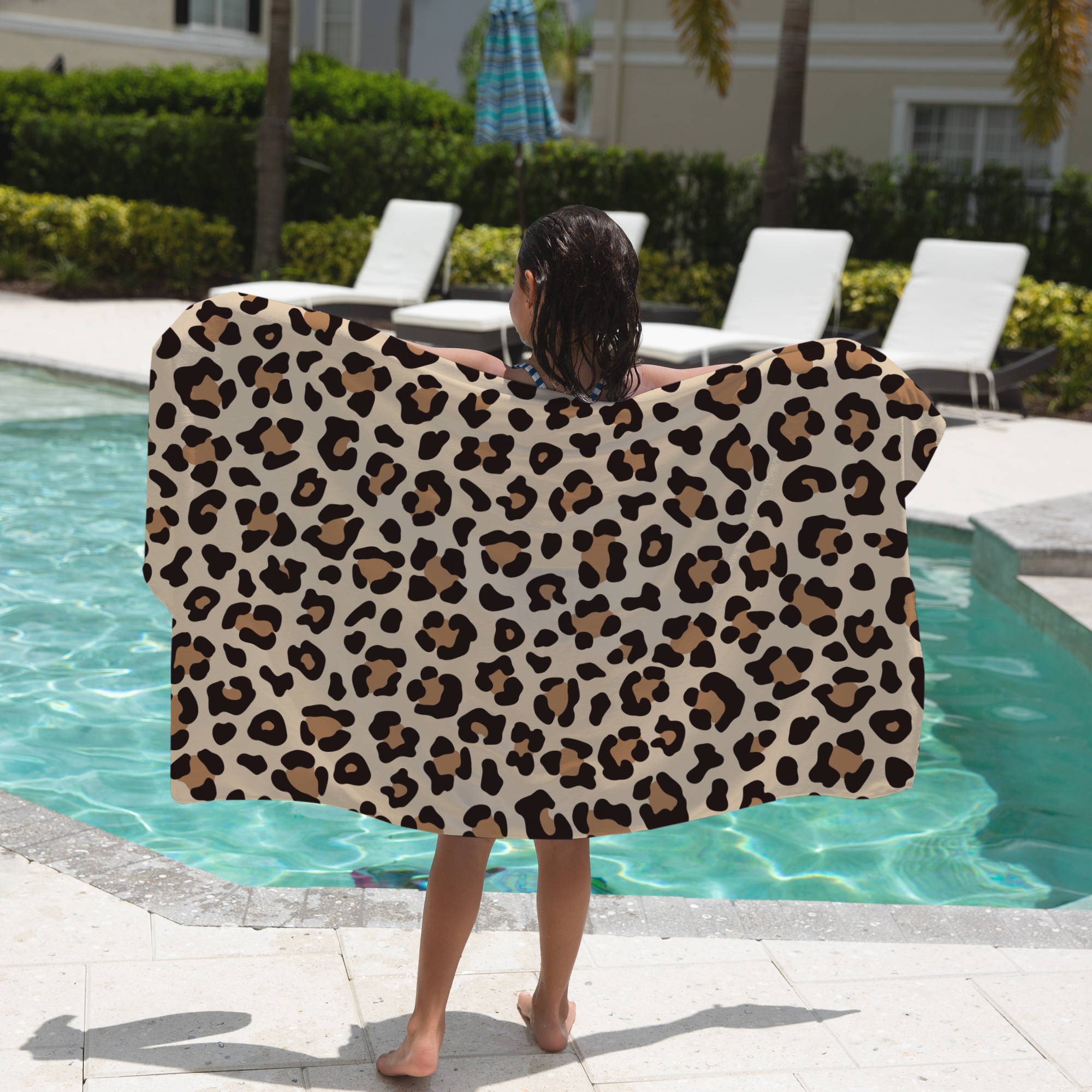 Child holding a leopard print towel by a pool