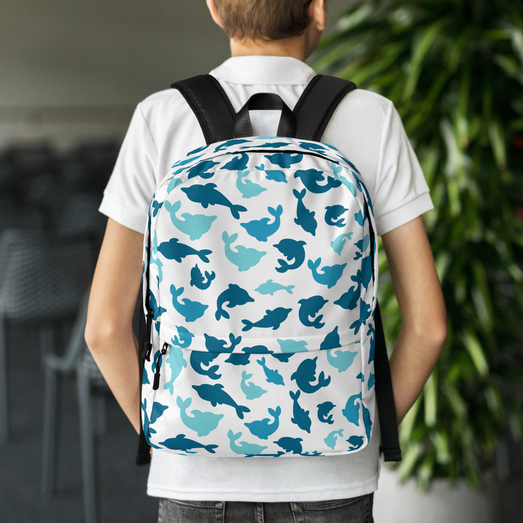White kids dolphin print backpack with blue and teal dolphin pattern and black straps shown from the back side