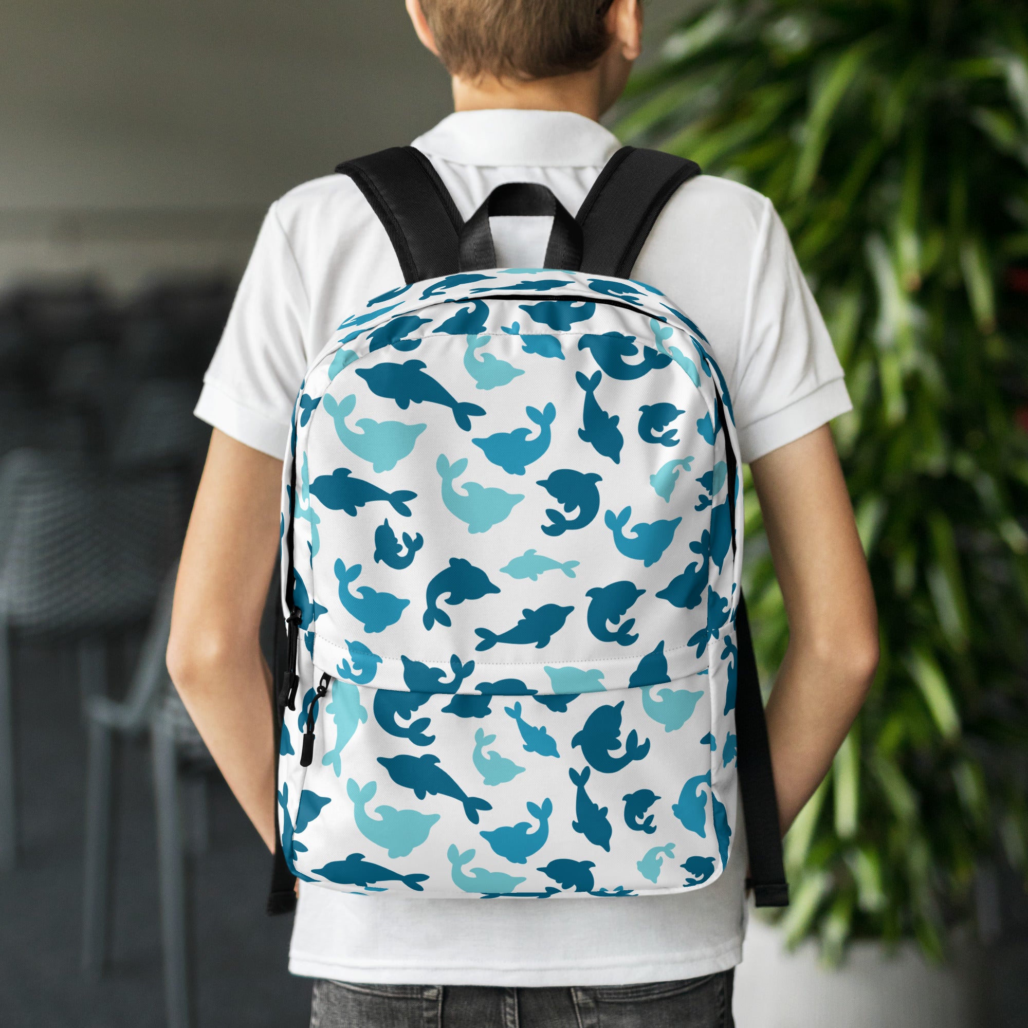 White kids dolphin print backpack with blue and teal dolphin pattern and black straps shown from the back side