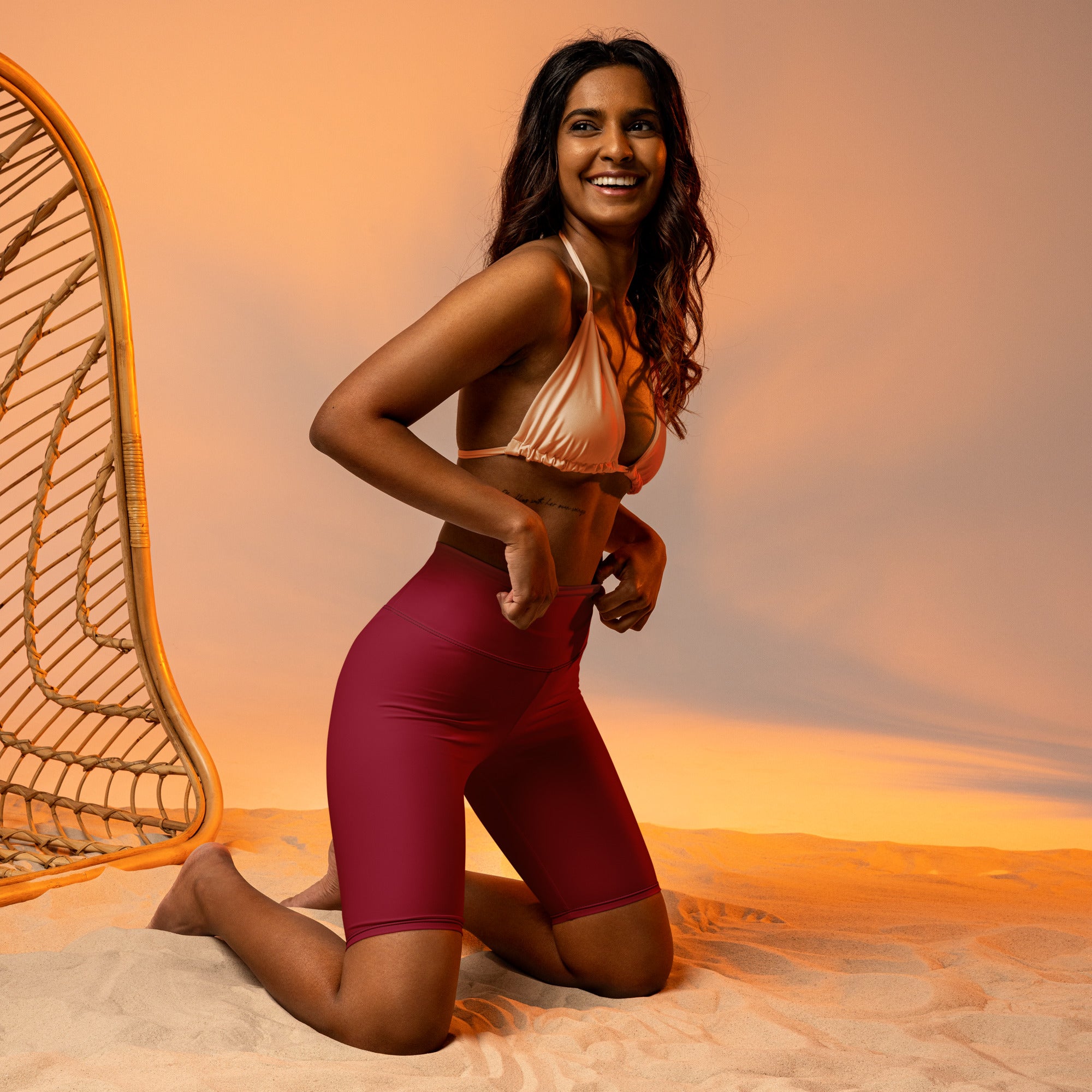A woman wearing women’s burgundy high waisted biker shorts with moisture wicking active fit and a metallic peach bikini top