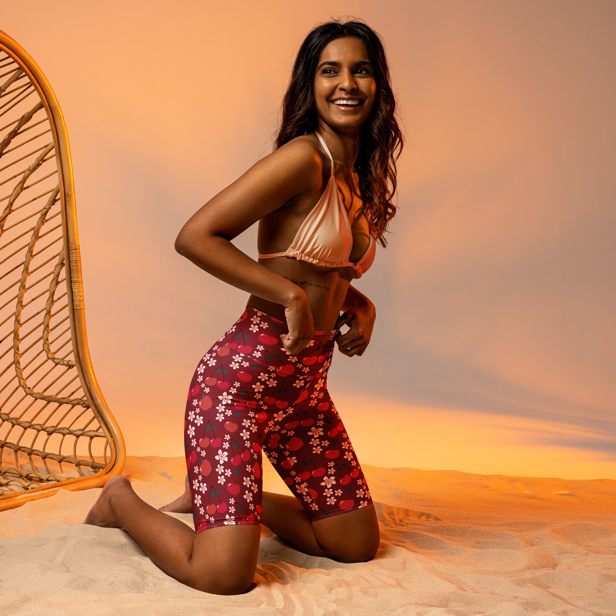 A woman wearing moisture wicking women’s burgundy cherry daisy high waisted biker shorts and a shiny peach halter top