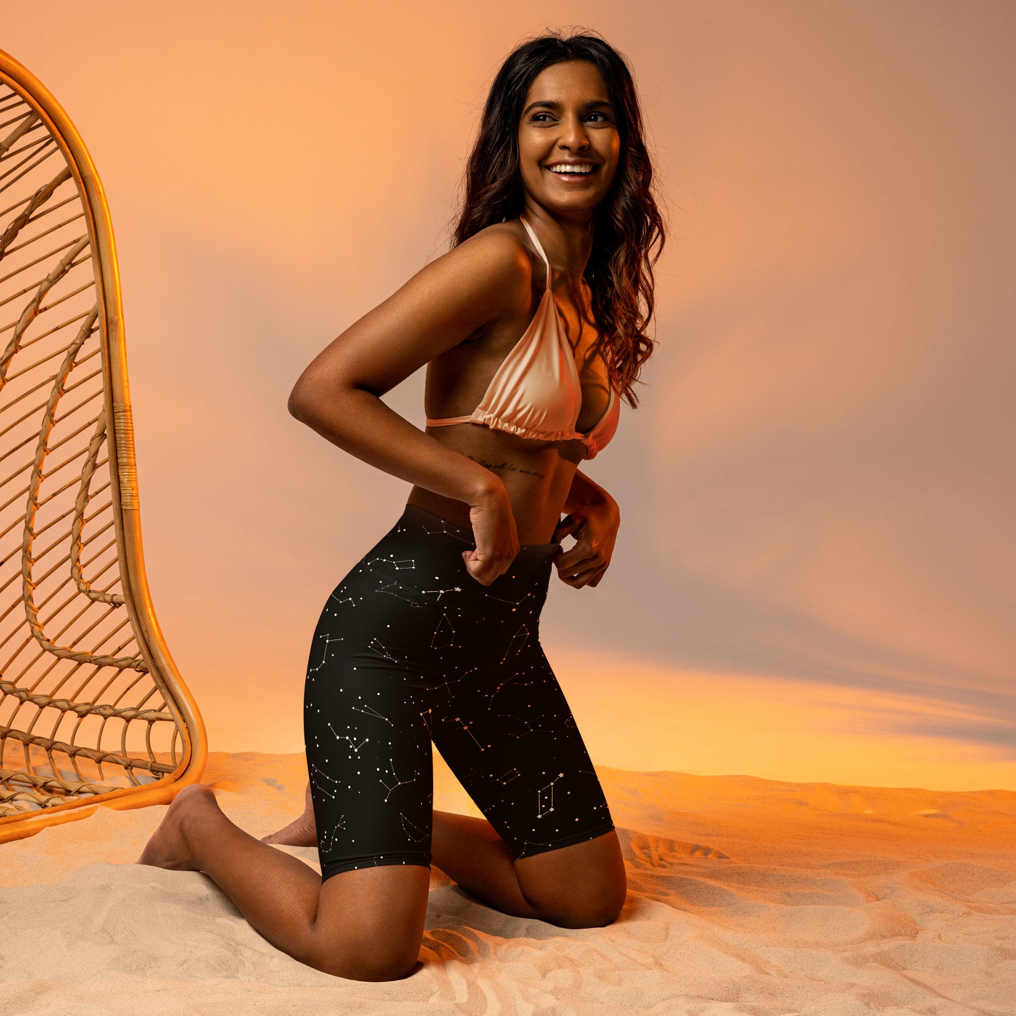 Black high waisted biker shorts with realistic constellation pattern and moisture wicking fabric paired with shiny peach halter top