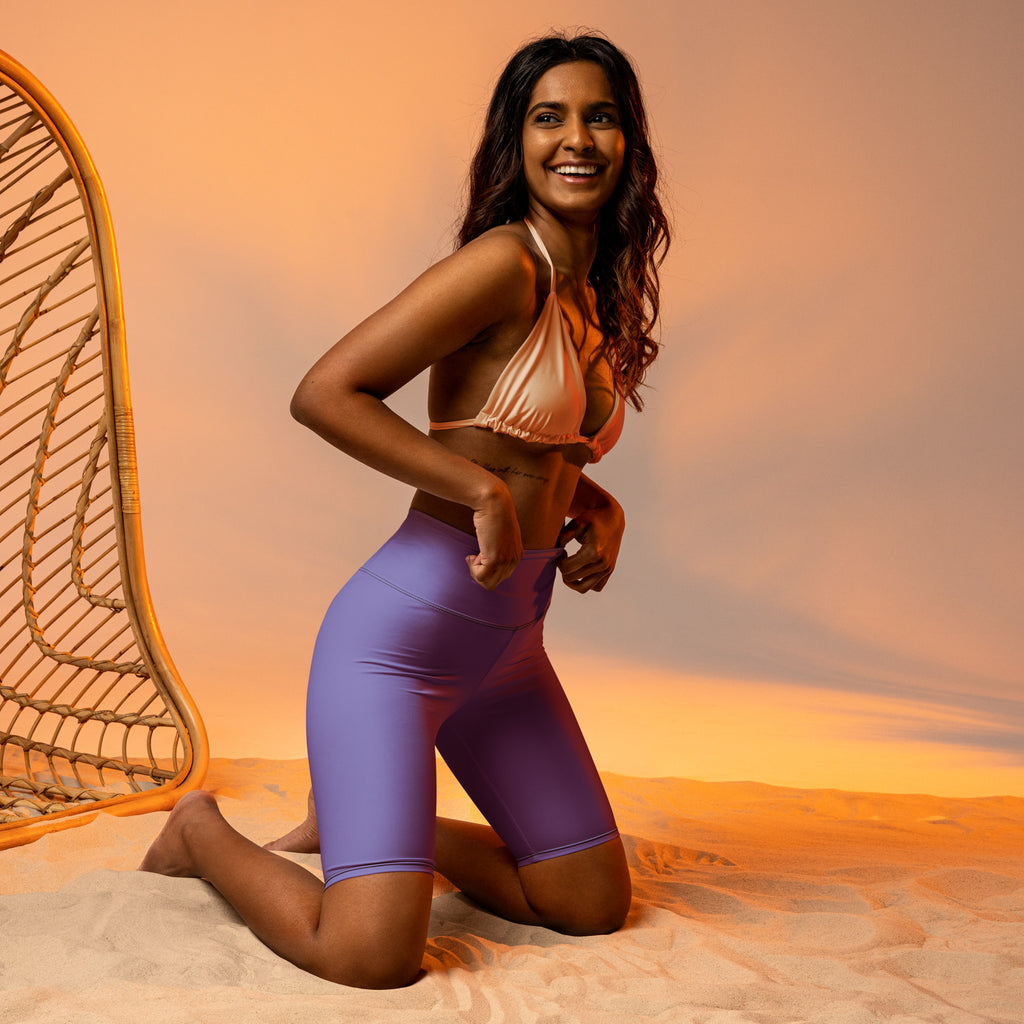 The model wears women’s purple high waisted biker shorts with moisture wicking fabric paired with a peach halter top
