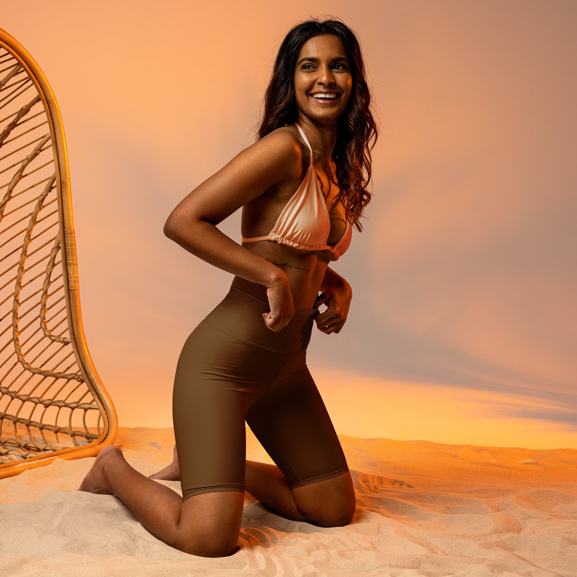 A shimmering peach satin bikini top with delicate halter straps paired with brown high waisted moisture wicking biker shorts