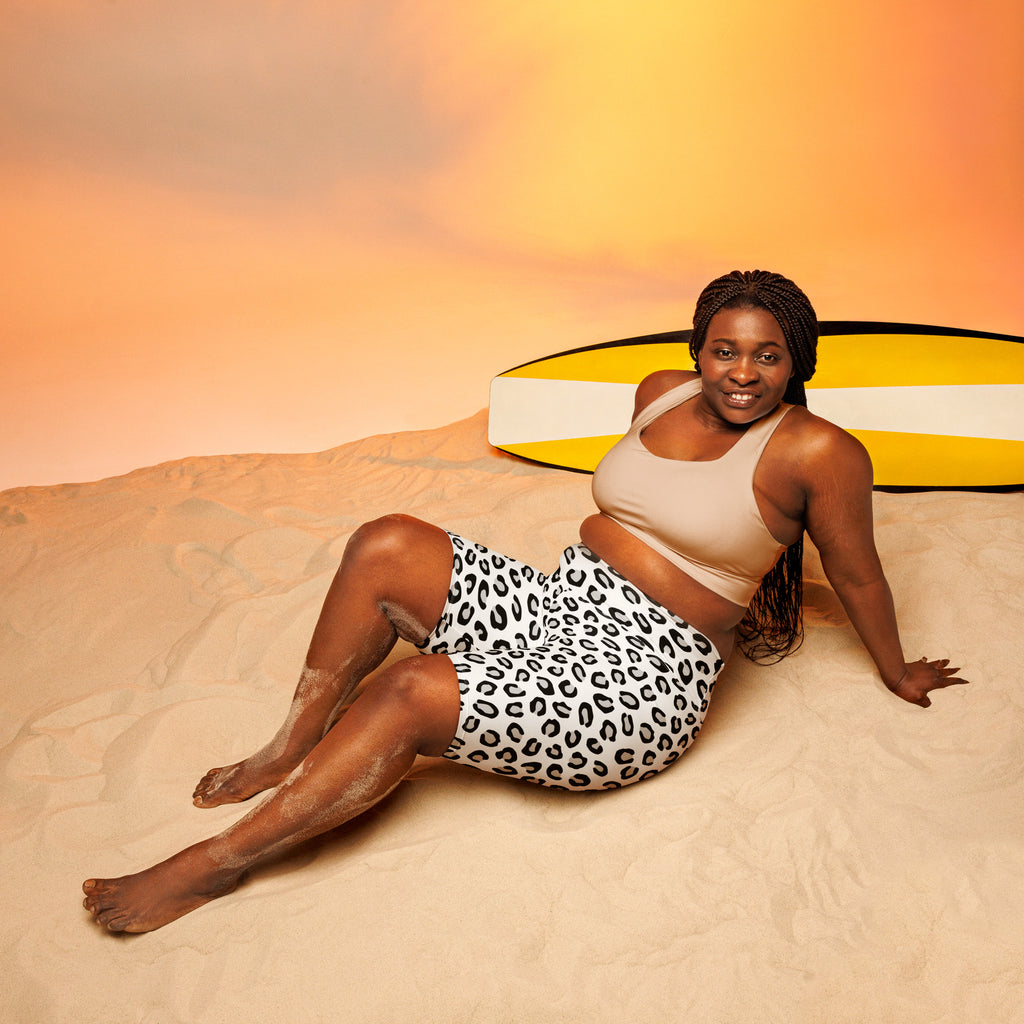 A woman reclining on sand wearing white leopard high waisted biker shorts with moisture wicking active fit