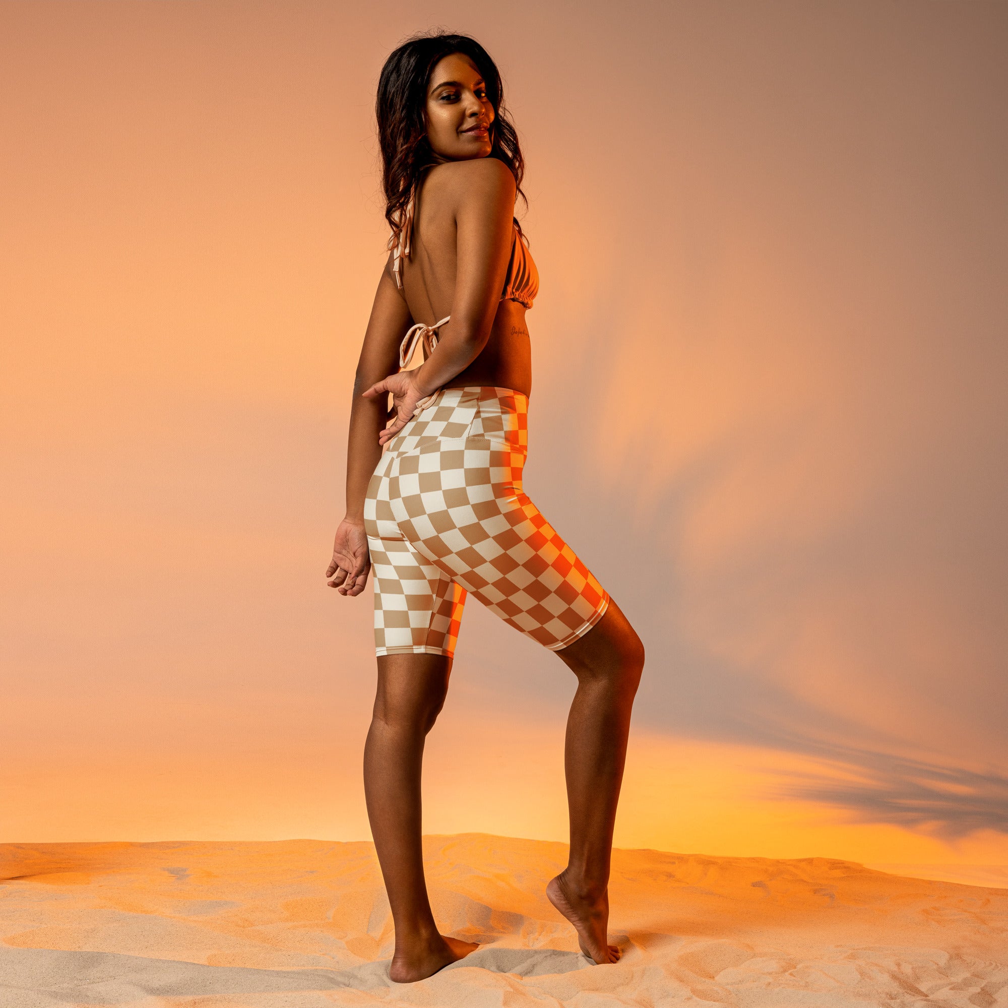 A woman wearing a beige and white checkered two-piece swimsuit with a tie-back top and high waisted moisture wicking biker shorts