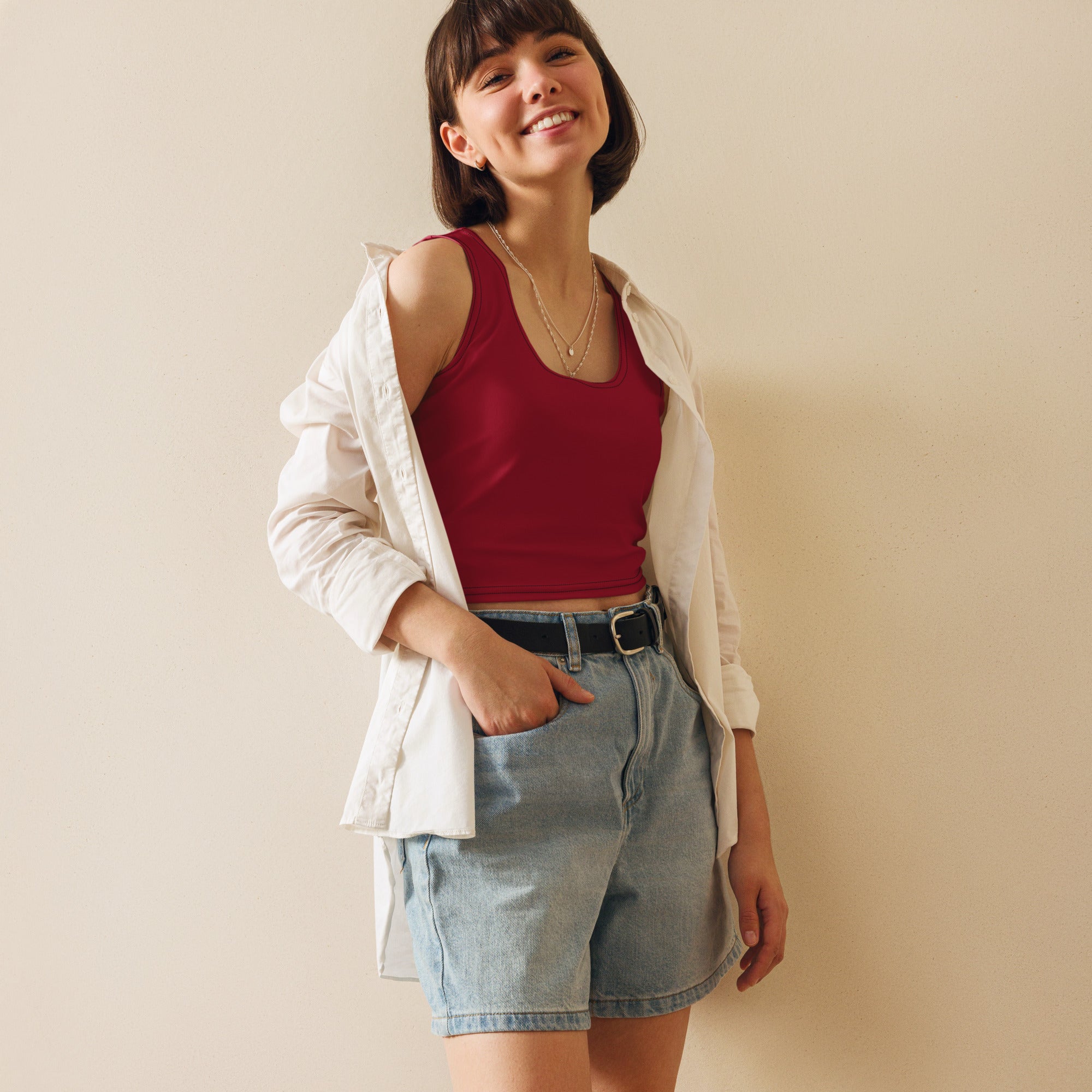 A woman wearing a women’s dark red buttery soft crop top in a red tank top style with light-wash denim shorts