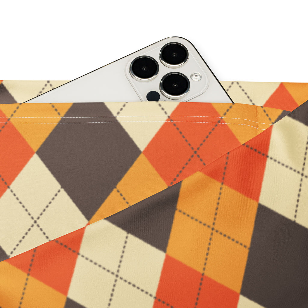 A white iphone with triple camera peeking from an orange beige and dark gray argyle fabric pouch in women’s fall high waist flare leggings