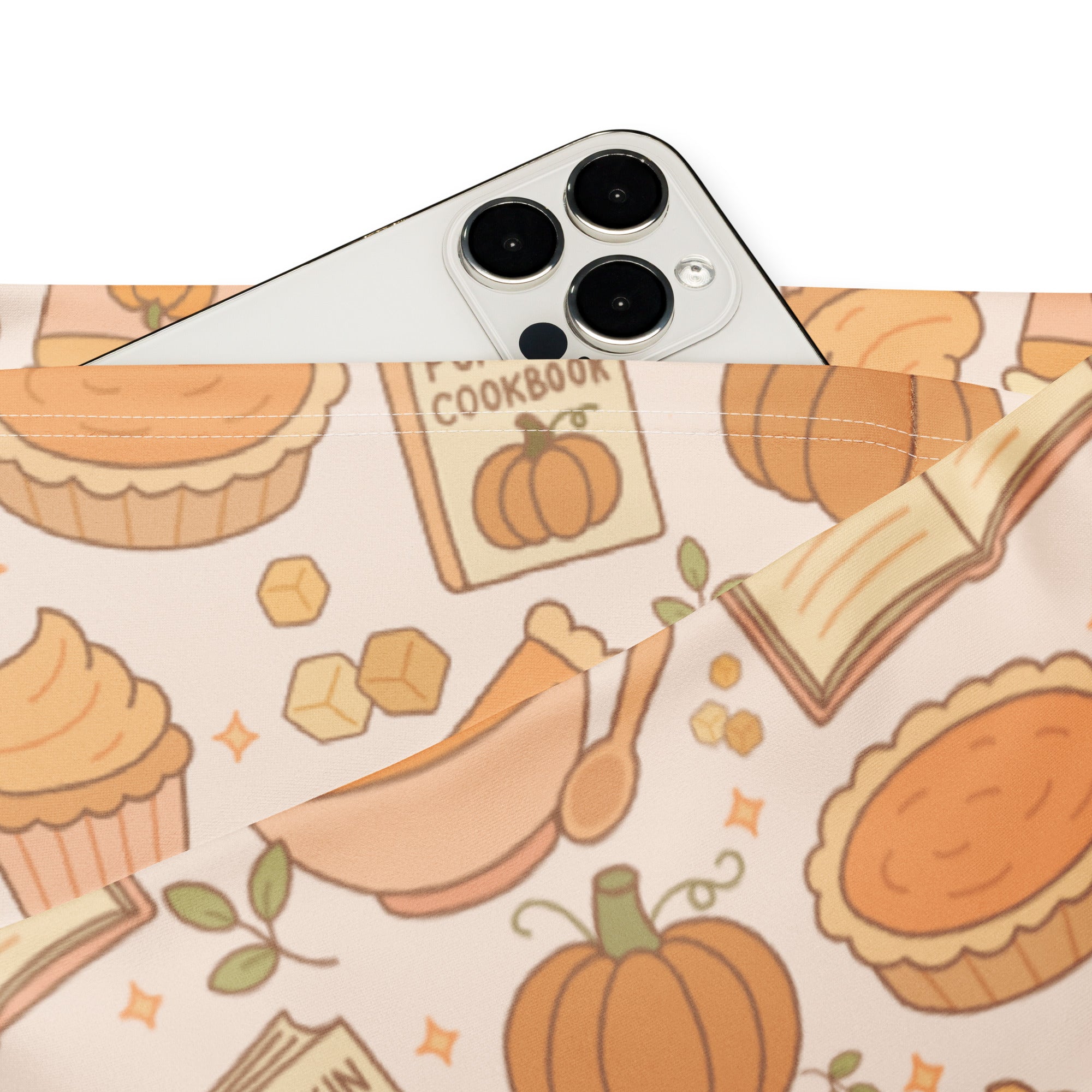 A white iphone with triple-camera rests on a fabric pouch featuring warm orange pumpkin pie themed high waist flare leggings