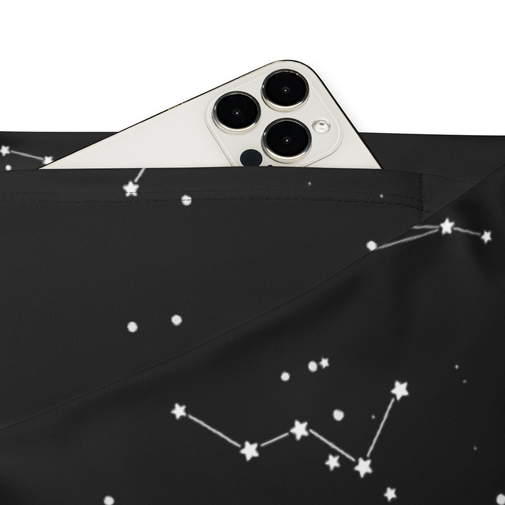 Black fabric women’s high waist flare legging pants with white star and constellation patterns and a silver iphone visible