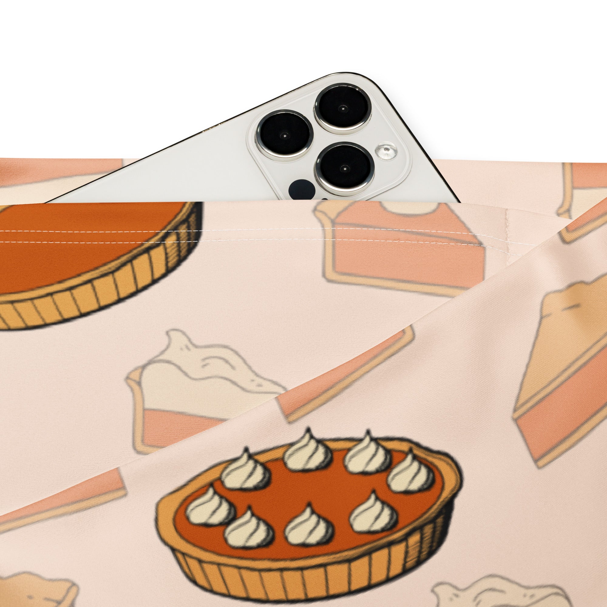 A white iphone with triple-camera rests on a light pink pumpkin pie pouch beside women’s pumpkin pie thanksgiving leggings