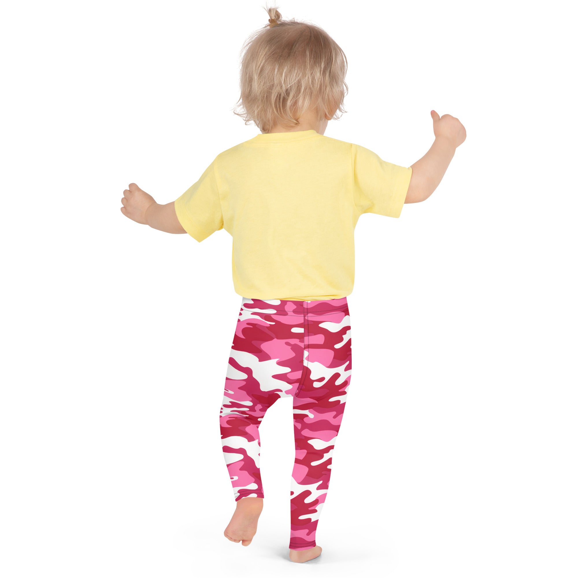 A toddler wearing girls pink camouflage buttery soft leggings and a yellow short-sleeved shirt standing upright