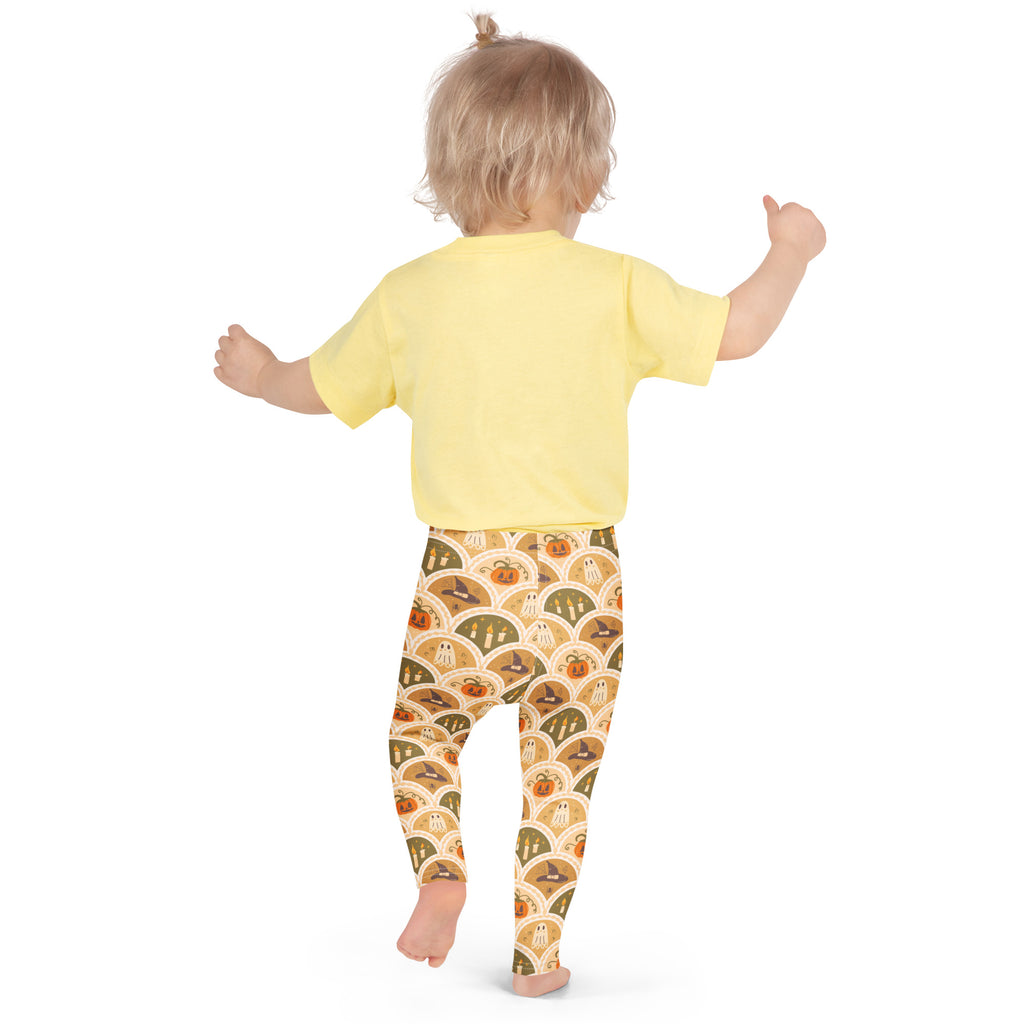 Kids autumn themed halloween buttery soft leggings in orange and beige with pumpkins ghosts and witches pattern paired with yellow short sleeve shirt
