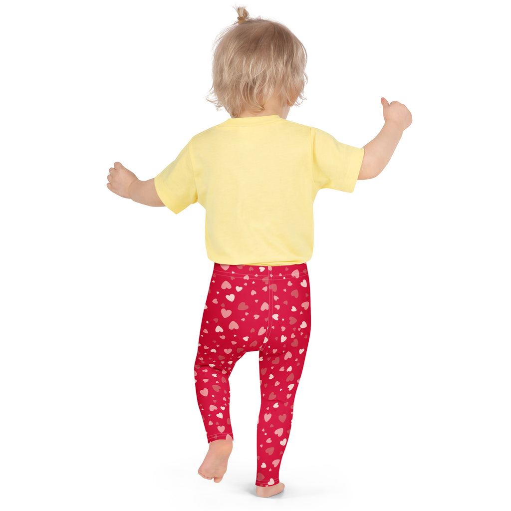 A child wearing girls red heart print buttery soft leggings with white and pink heart patterns on red fabric