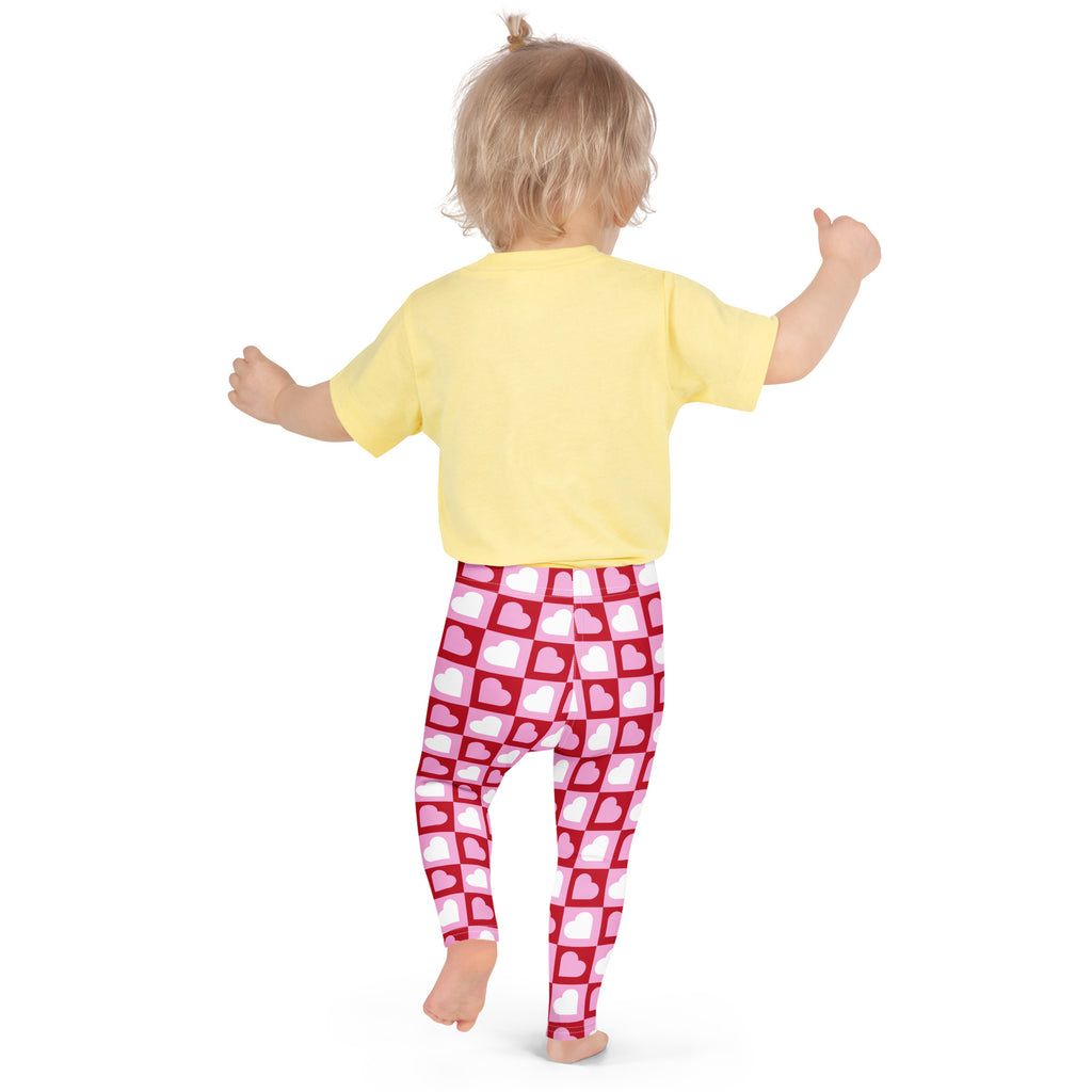 A child wearing girls pink checkered heart buttery soft red leggings with white hearts and a yellow short-sleeved shirt
