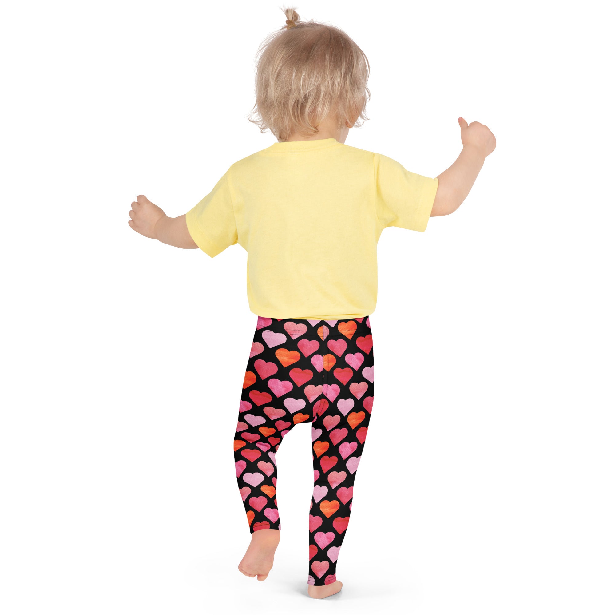 A child wearing girls black heart buttery soft leggings in black with colorful heart patterns and a yellow short-sleeved shirt