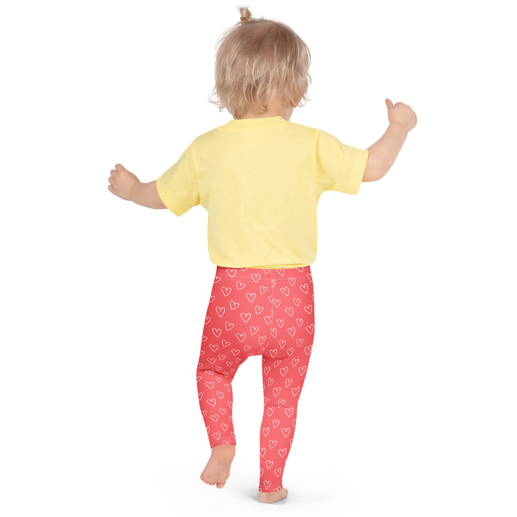 A child wearing girls pink heart outline buttery soft coral-red leggings with white hearts and a yellow shirt