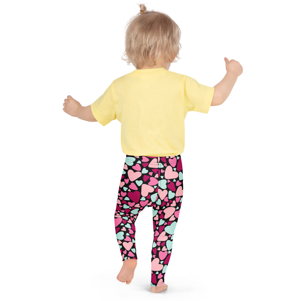A child wearing girls multicolor heart buttery soft leggings and a yellow short-sleeved shirt standing front view