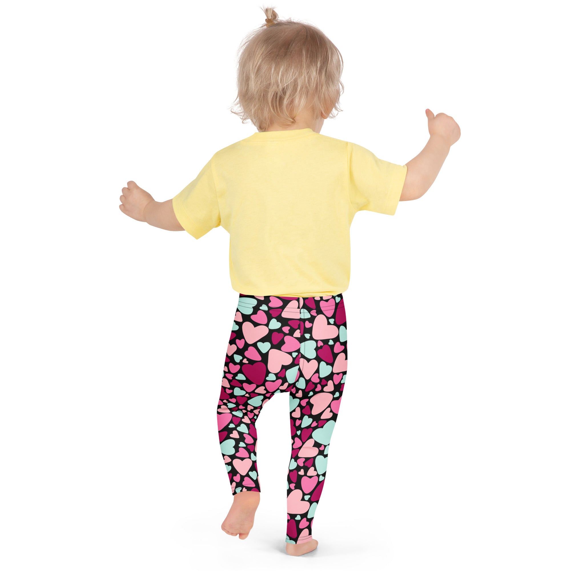 A child wearing girls multicolor heart buttery soft leggings and a yellow short-sleeved shirt standing front view