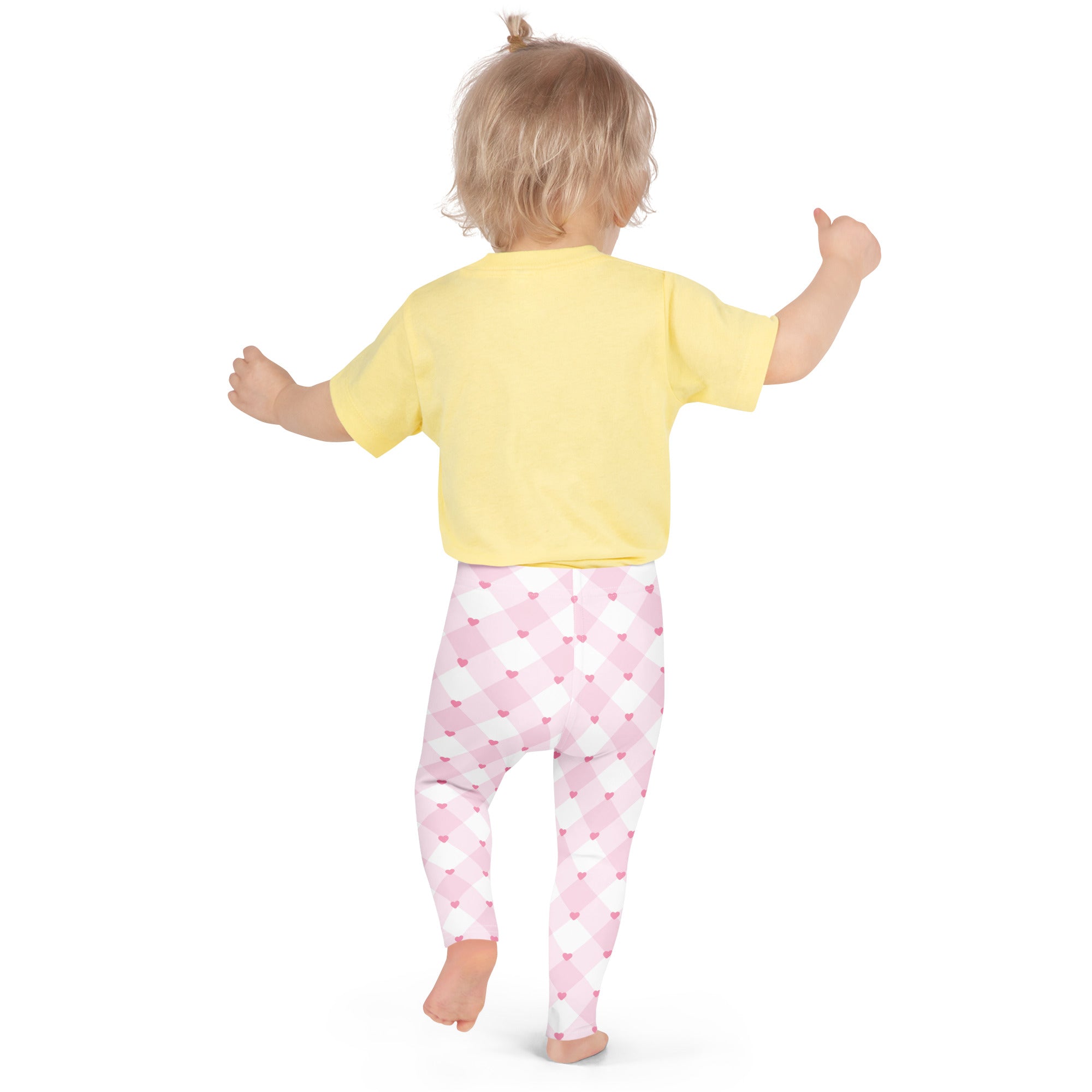 A child wearing girls pink gingham heart buttery soft leggings in pink white heart pattern with a yellow top