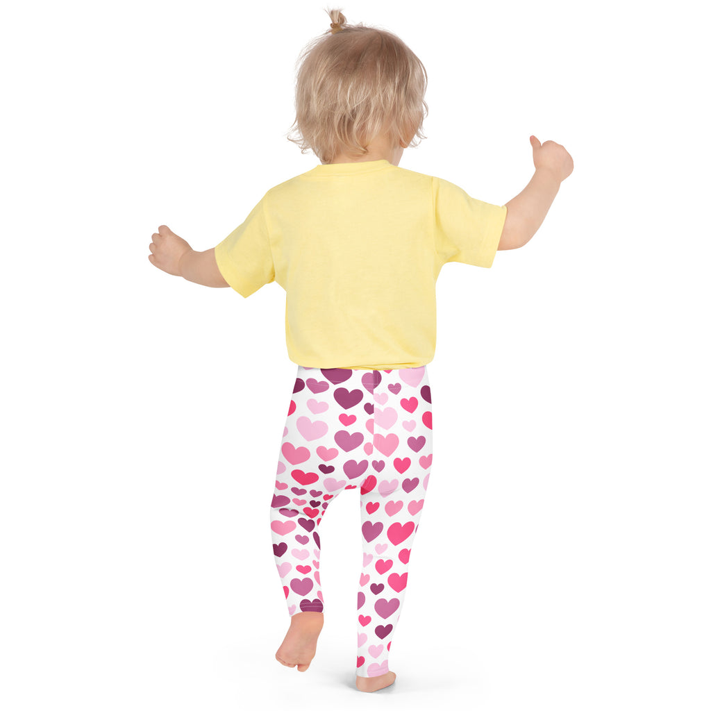 A child wearing buttery soft girls leggings in white with purple and pink heart patterns and a yellow short-sleeved shirt