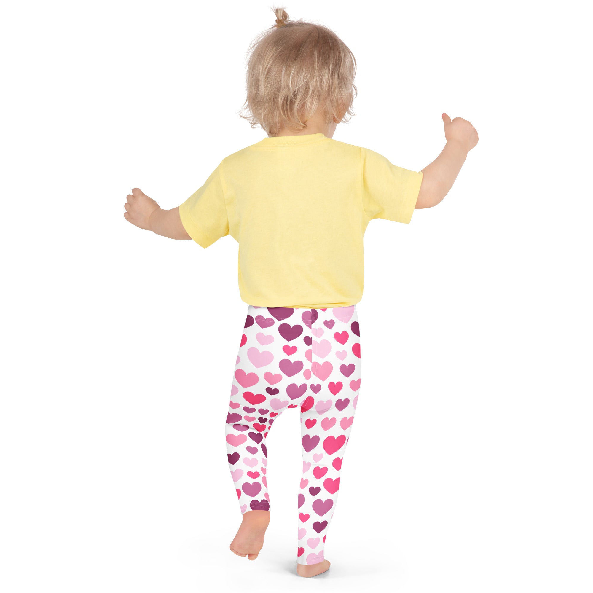 A child wearing buttery soft girls leggings in white with purple and pink heart patterns and a yellow short-sleeved shirt