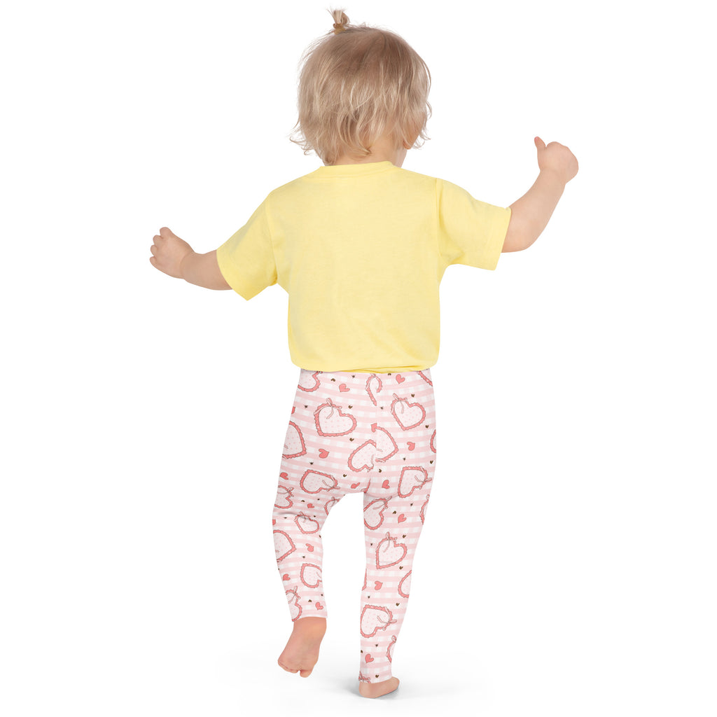 A child wearing girls plaid bow heart buttery soft leggings in pink with white stripes and red heart patterns