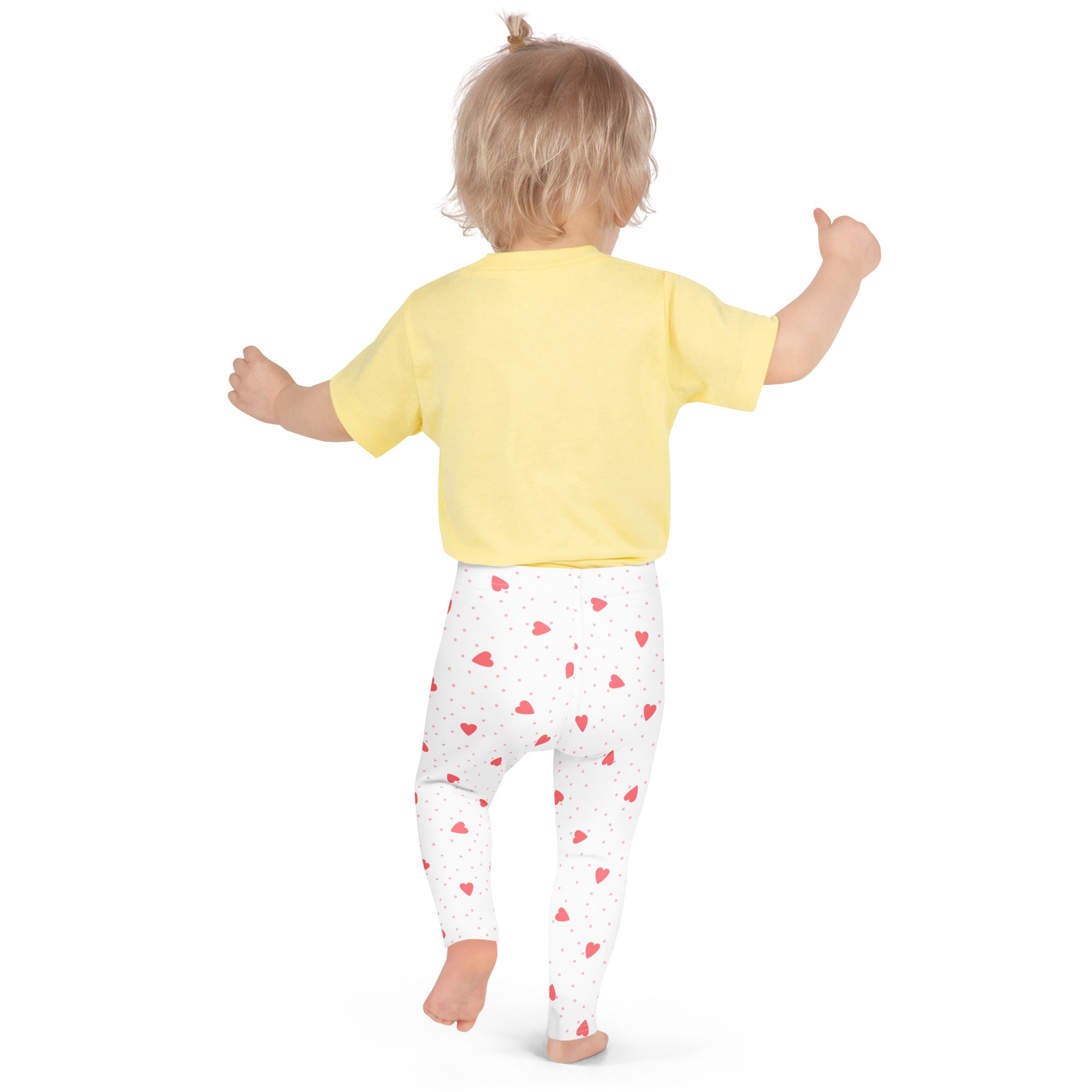 A toddler wearing girls scattered heart leggings buttery soft white leggings with red heart patterns and a yellow top