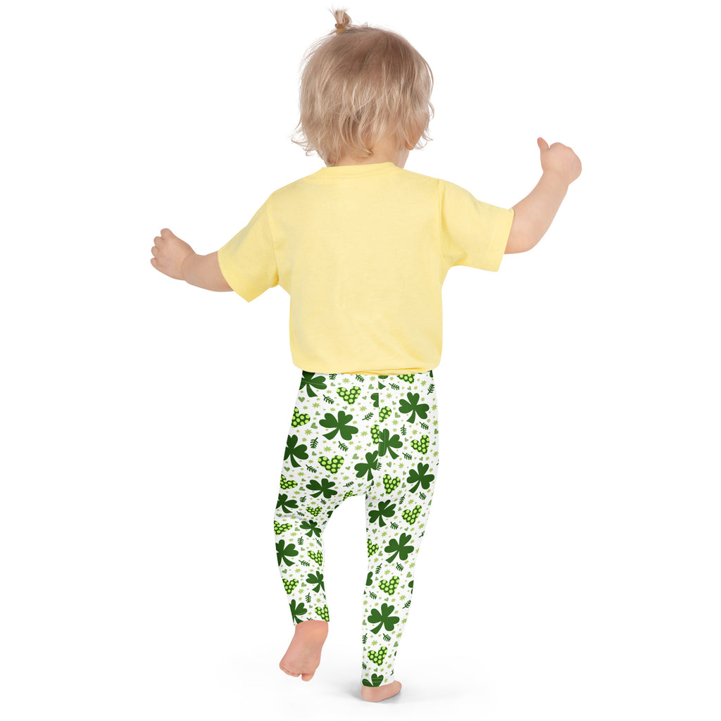 A child wearing buttery soft girls shamrock and heart leggings in white with green patterns and a yellow short sleeve shirt