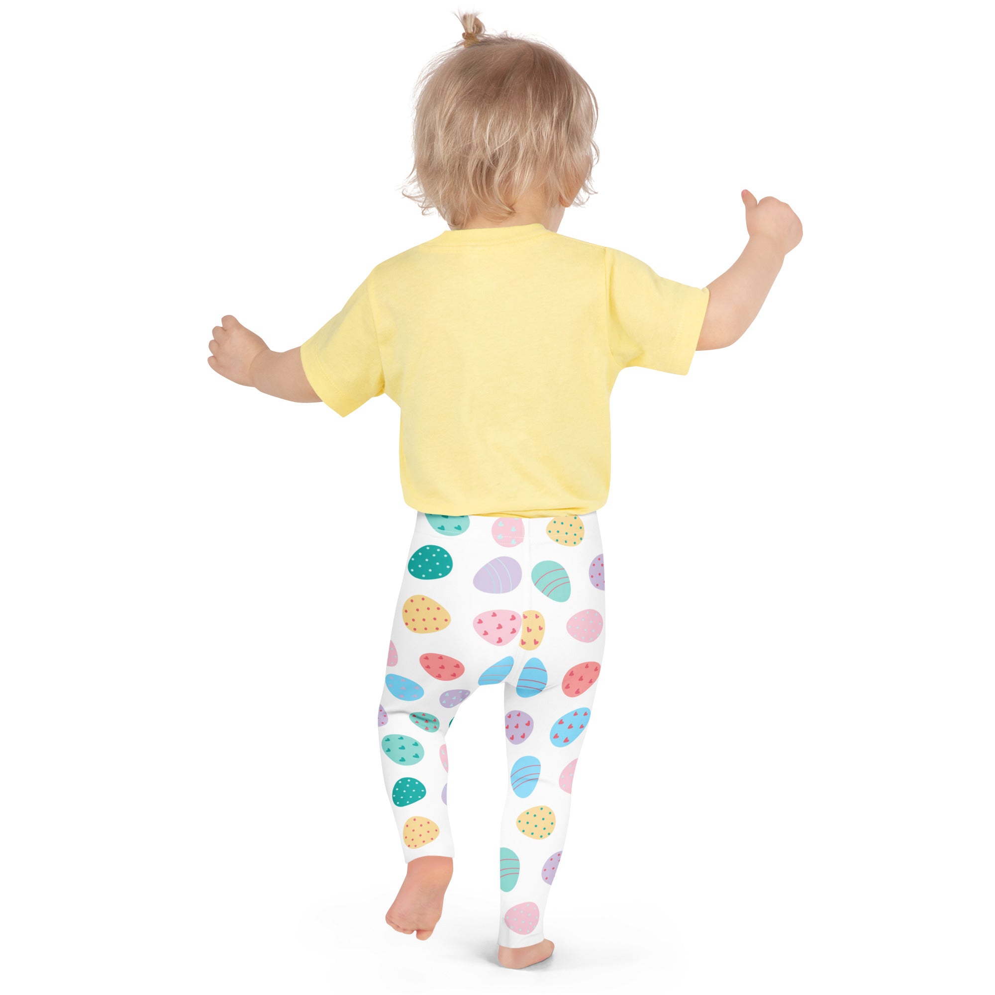 A child wearing pastel easter egg buttery soft white leggings with colorful patterns and a yellow short-sleeved shirt