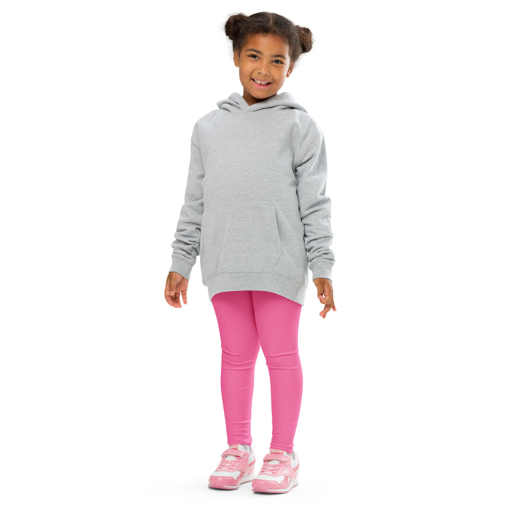Smiling girl in a grey hoodie and pink leggings, standing against a white background