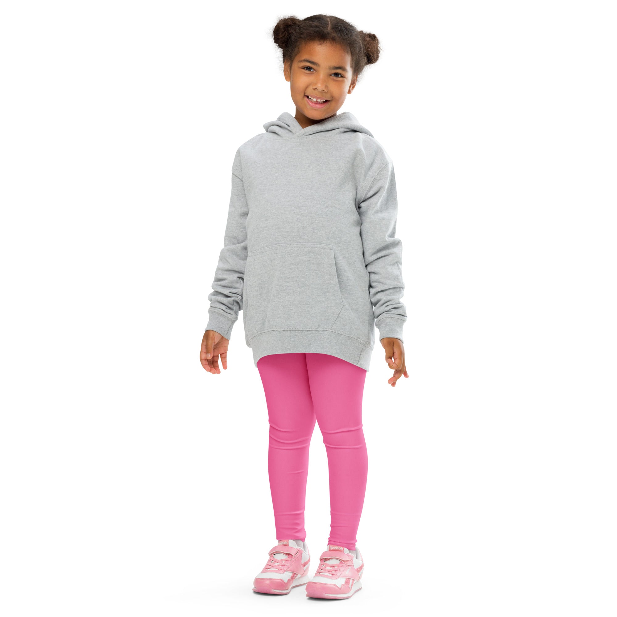 Smiling girl in a grey hoodie and pink leggings, standing against a white background