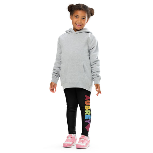 Smiling girl in a grey hoodie and black personalized kids leggings with rainbow name print