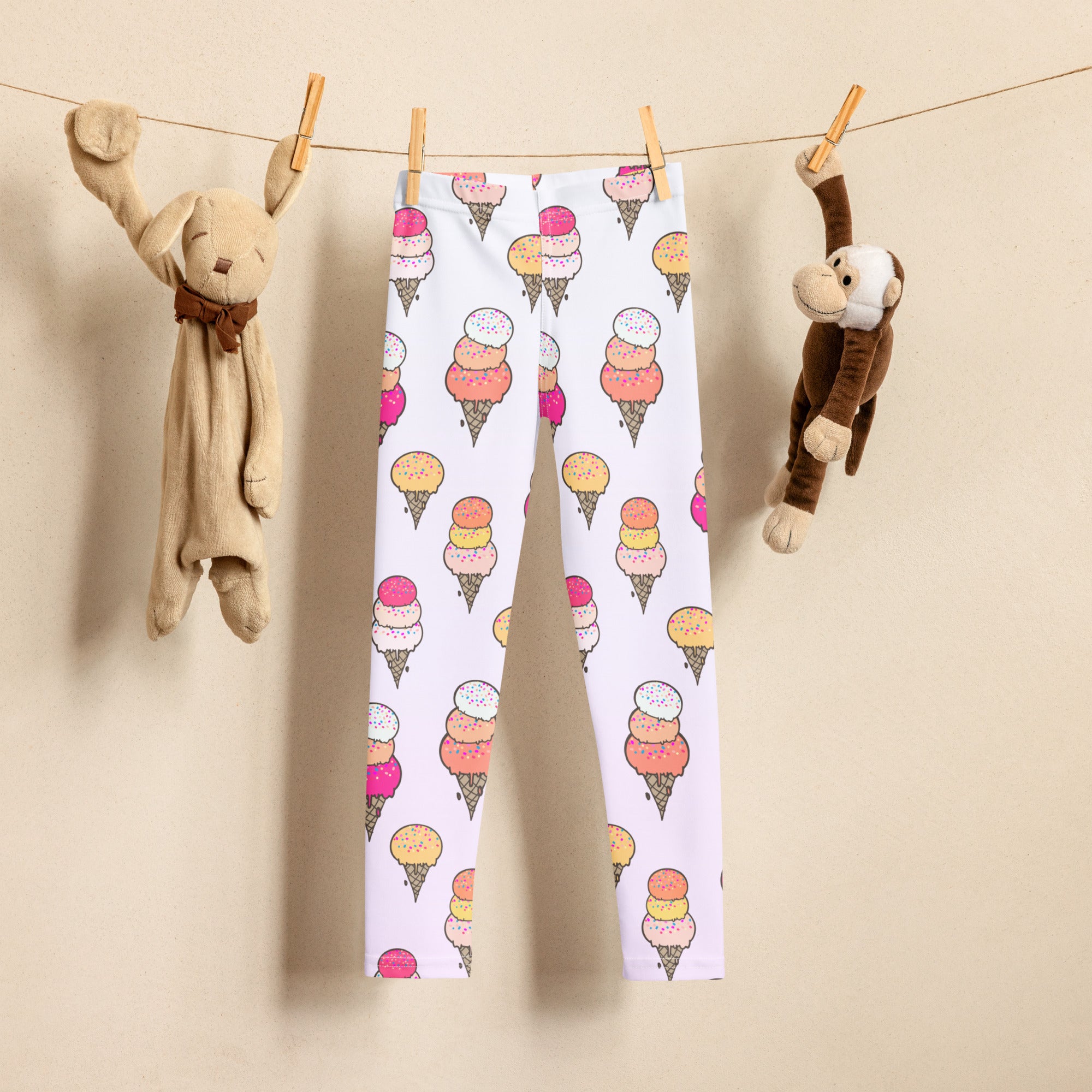 Kids leggings with colorful ice cream cone print hanging on a line between two plush toys