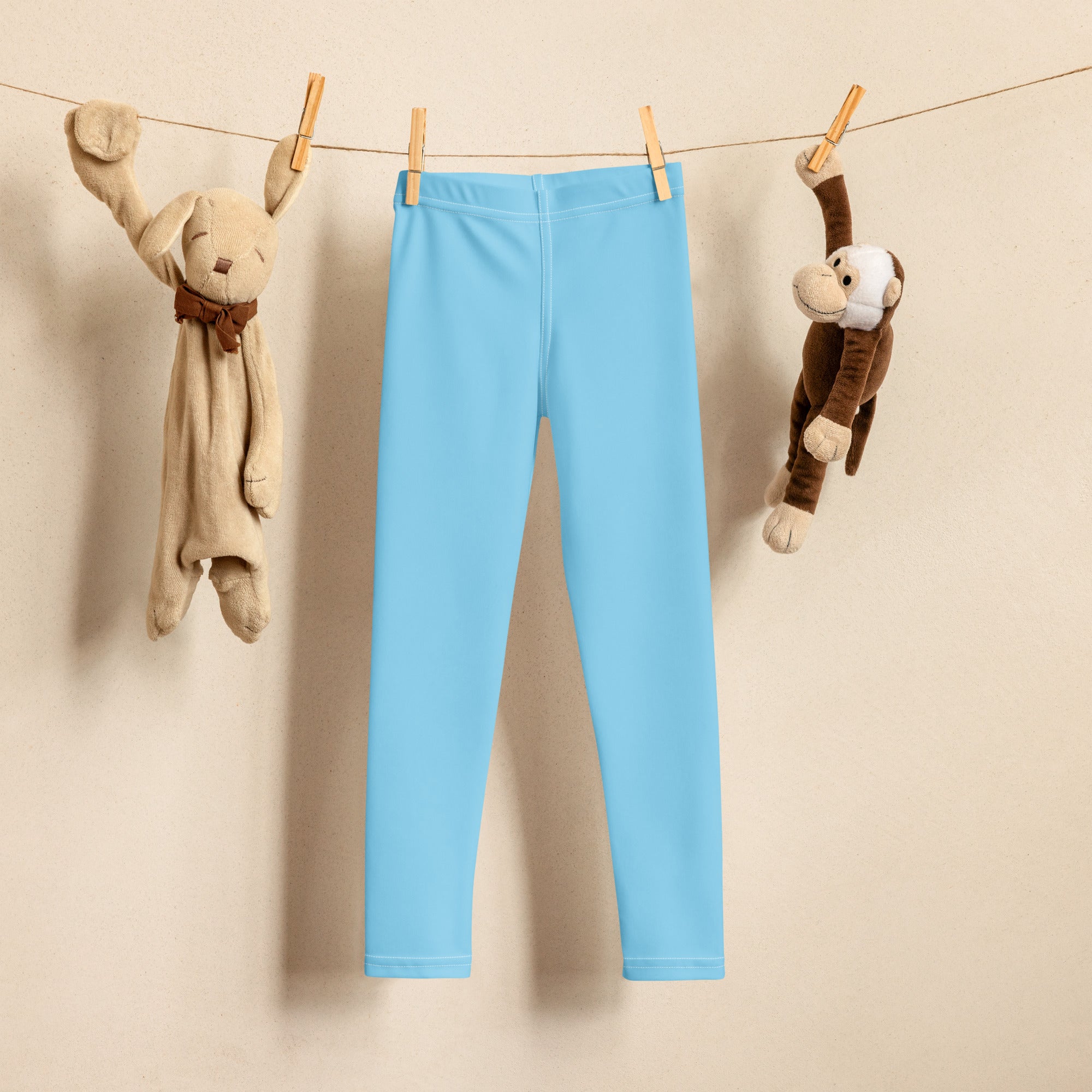 Kids buttery soft sky blue leggings made of stretchy fabric hanging on a clothesline between two stuffed animals
