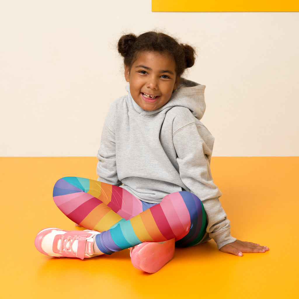 The girl is wearing girls bright rainbow striped buttery soft leggings with vibrant pink blue yellow and green diagonal stripes