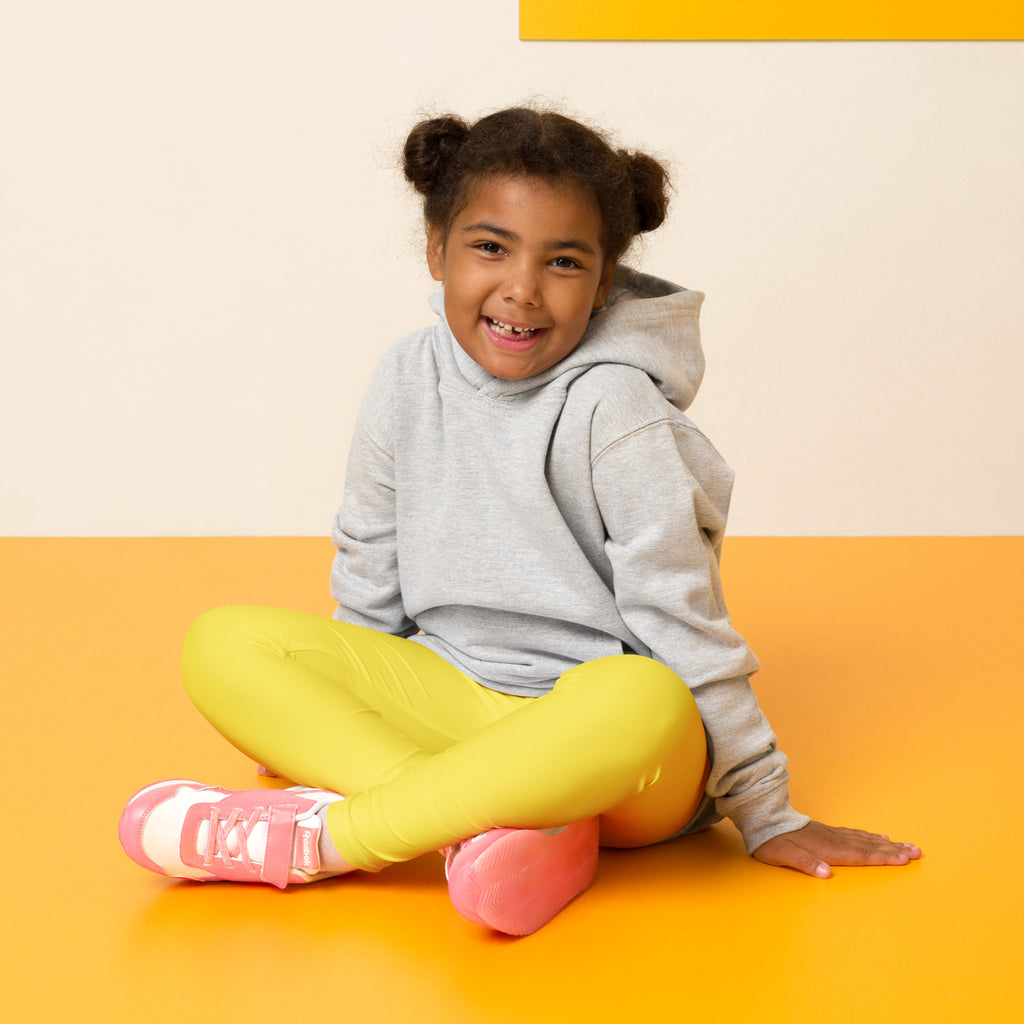A child wearing kids buttery soft yellow leggings with a gray hoodie and pink sneakers with white laces