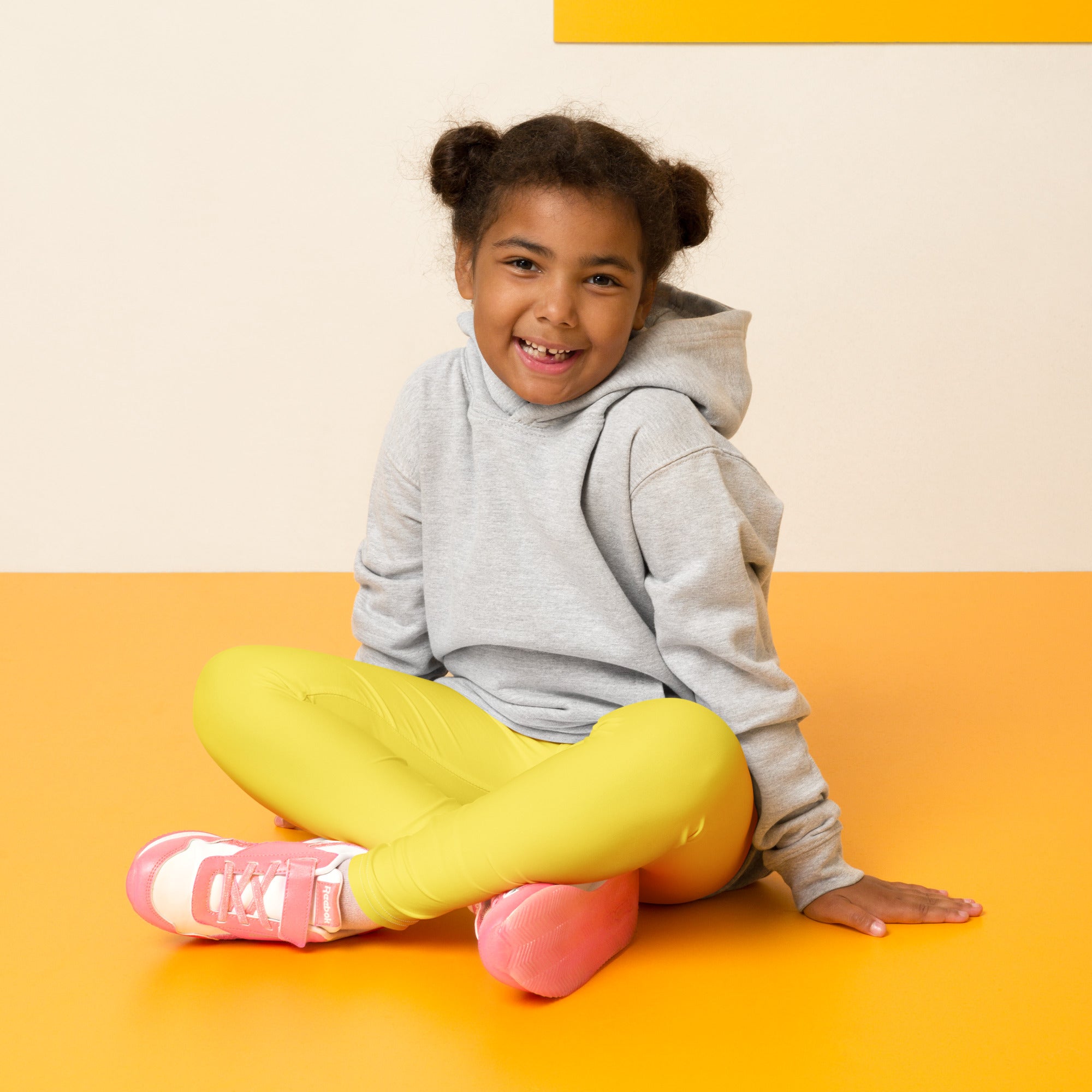 A child wearing kids buttery soft yellow leggings with a gray hoodie and pink sneakers with white laces