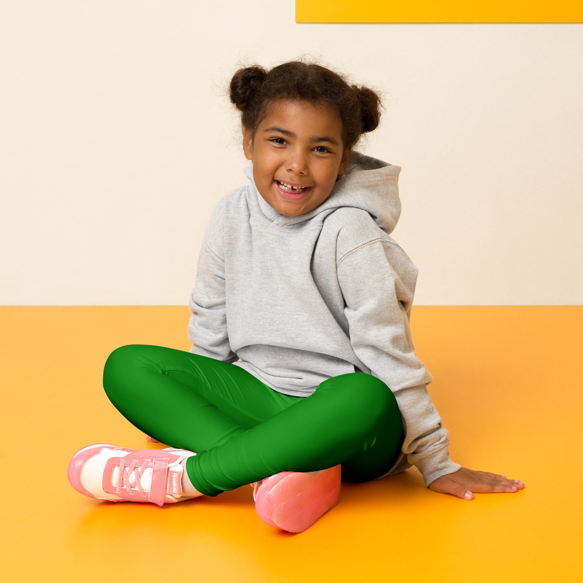 A child wearing kids buttery soft green leggings made of soft material paired with a gray hoodie and pink sneakers
