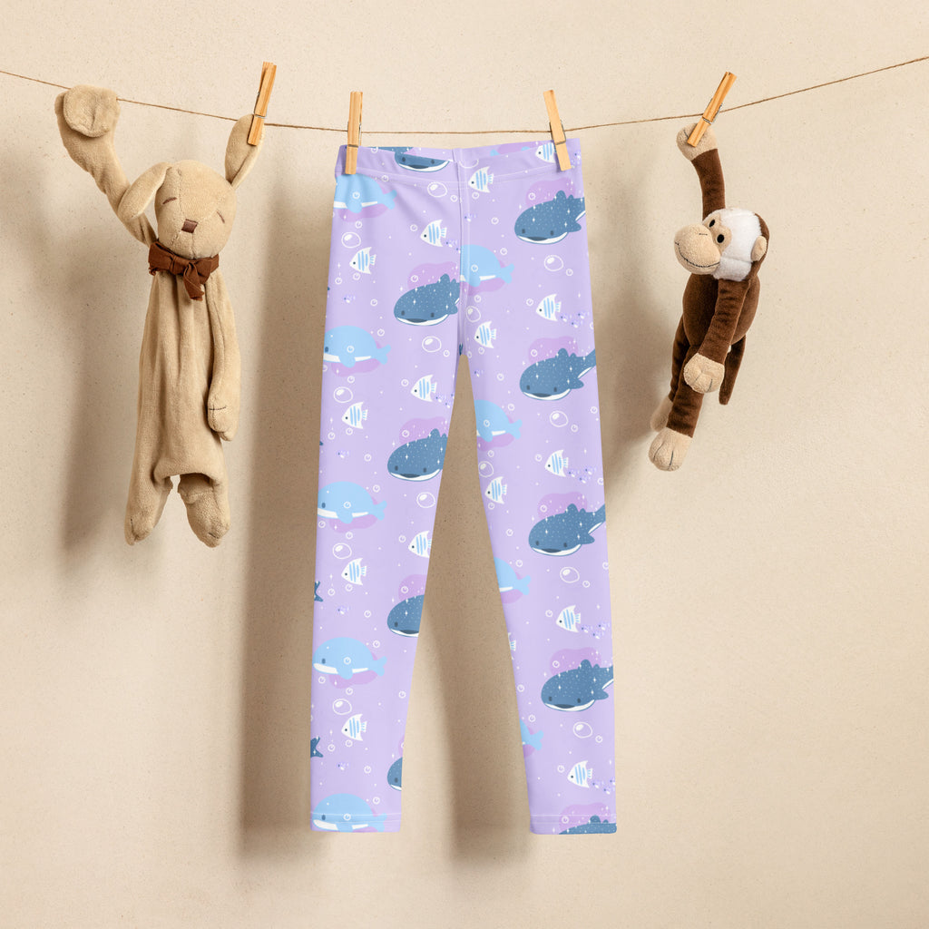 Girls purple buttery soft leggings with playful blue whale and small fish pattern hanging on clothesline between stuffed animals