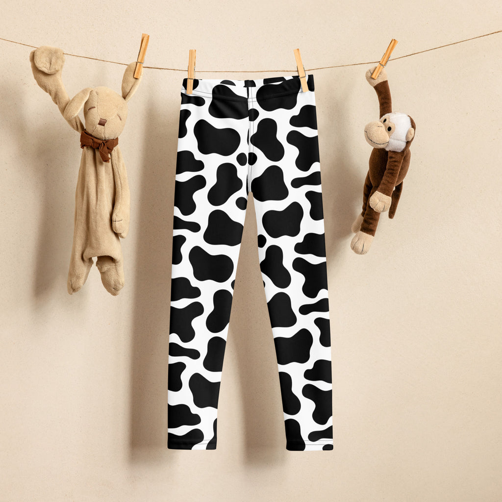 Kids cow print buttery soft black and white leggings hanging on a clothesline showing the front side