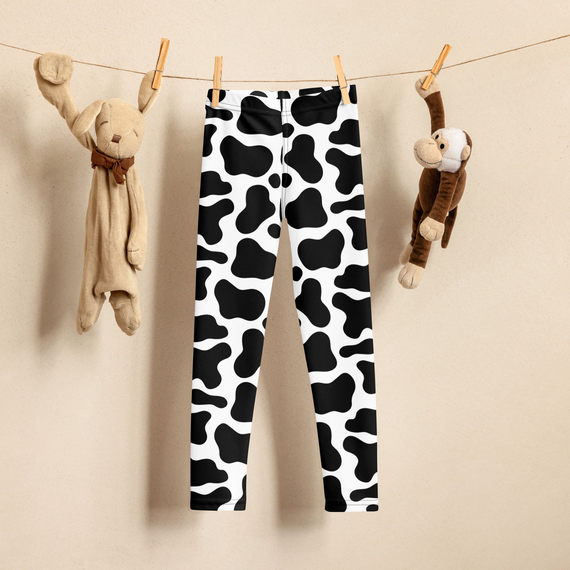 Kids cow print buttery soft black and white leggings hanging on a clothesline showing the front side