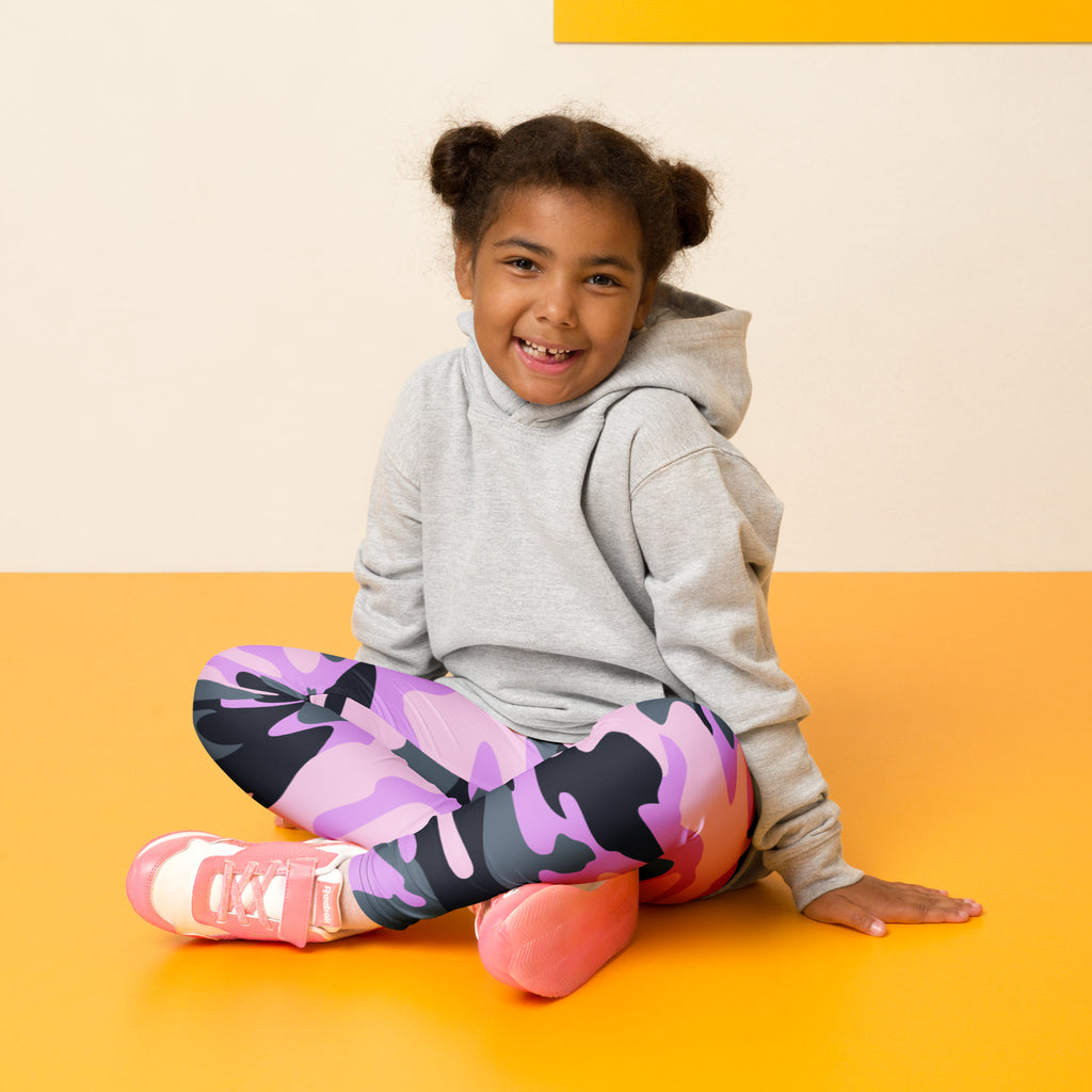 A young girl wearing girls purple camouflage buttery soft leggings with vibrant purple black and pink colors and matching pink sneakers