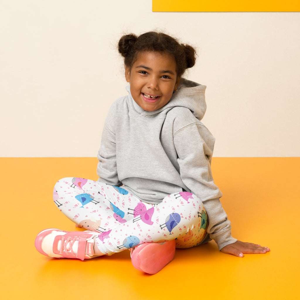 Girl wearing white buttery soft leggings with colorful pink blue and purple cartoon birds print