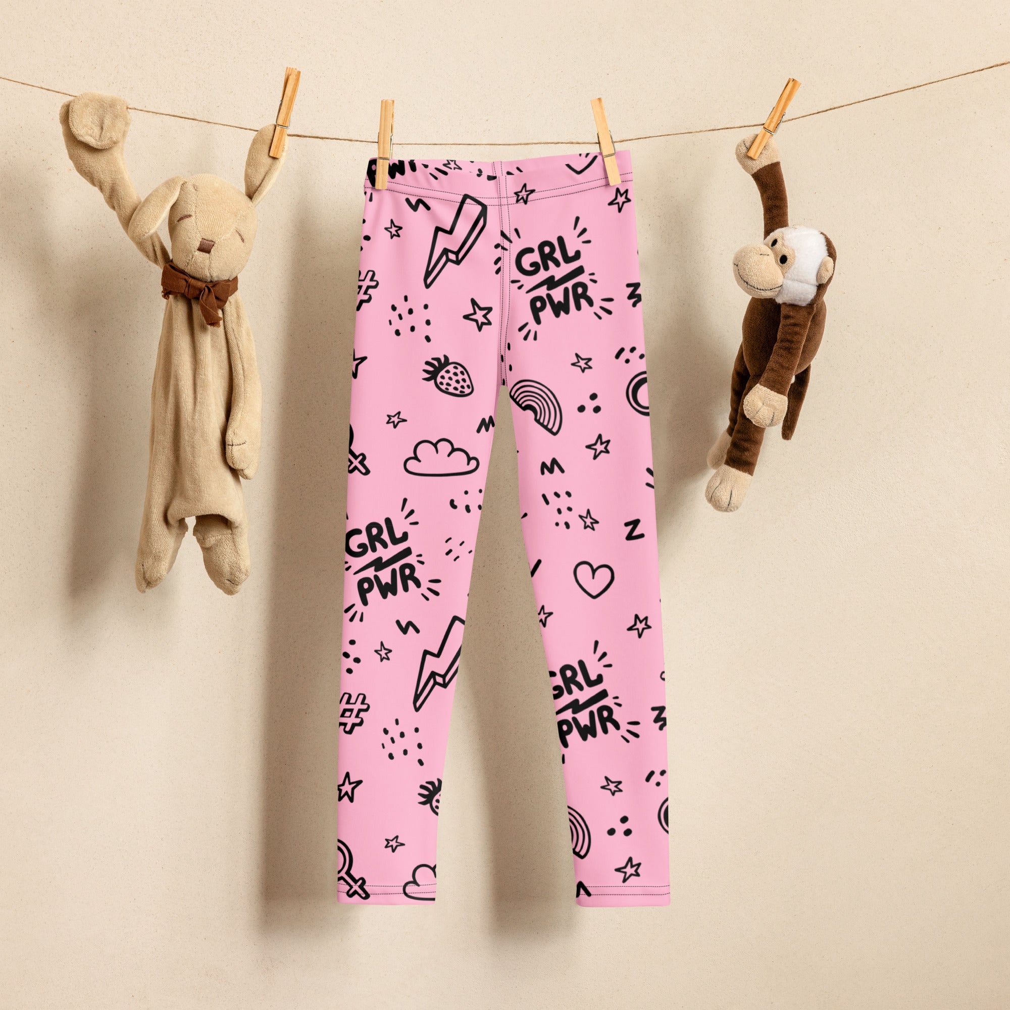 Pink buttery soft kids leggings with black grl pwr text and cartoon graphics hanging on a clothesline