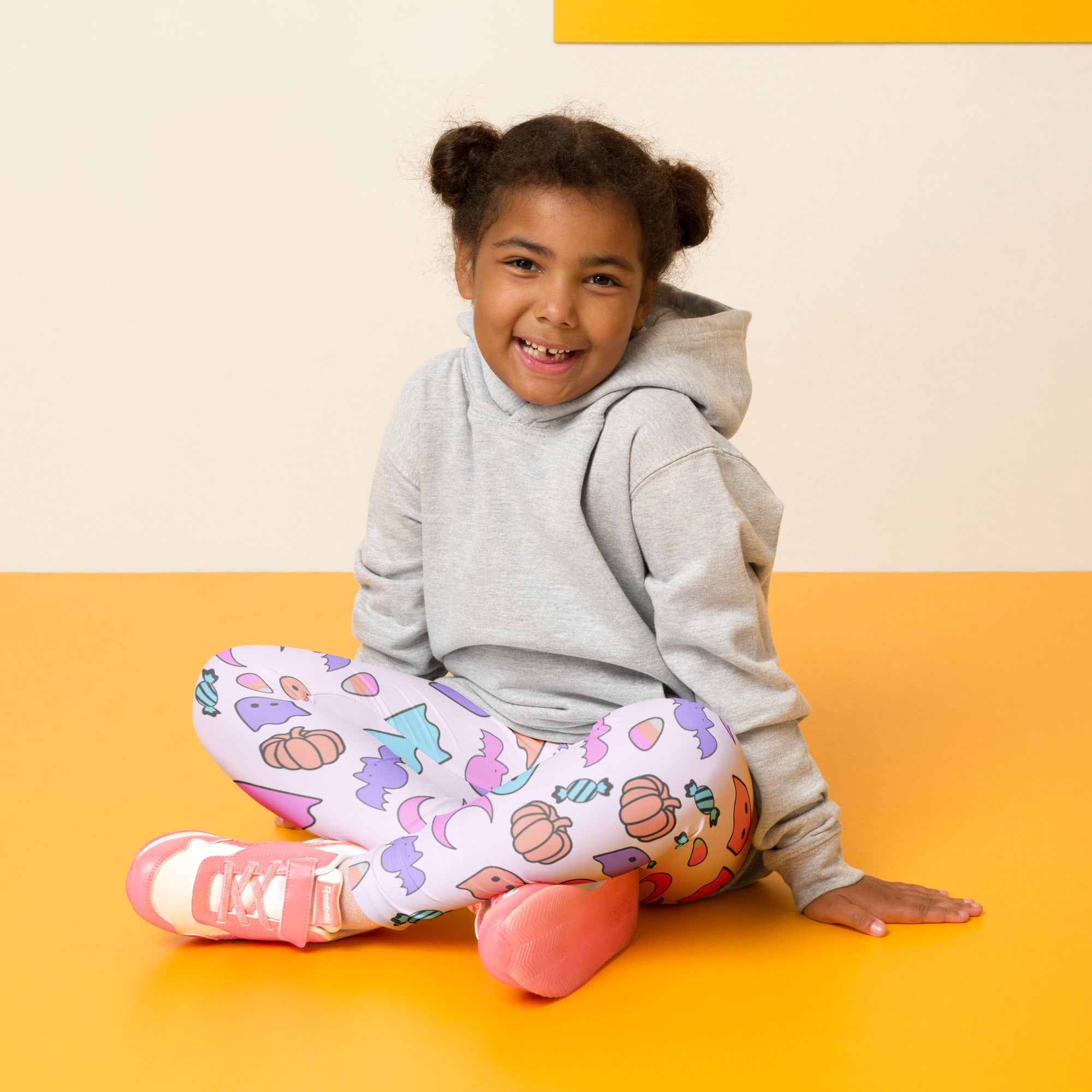 Girl wearing white buttery soft leggings with colorful halloween pumpkin bat and candy patterns