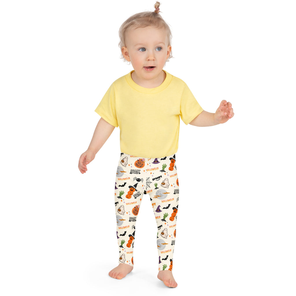 A child wearing buttery soft kids trick-or-treat halloween leggings with pumpkins bats ghosts and witch hats on off-white